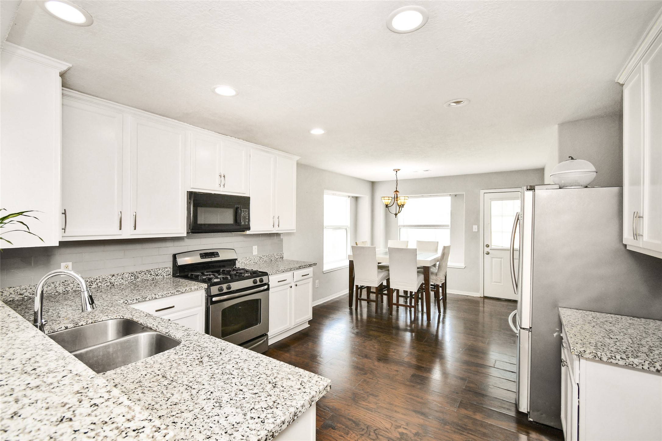 Beautifully updated kitchen with white cabinetry, granite countertops, and stainless steel appliances, opening to the dining area.