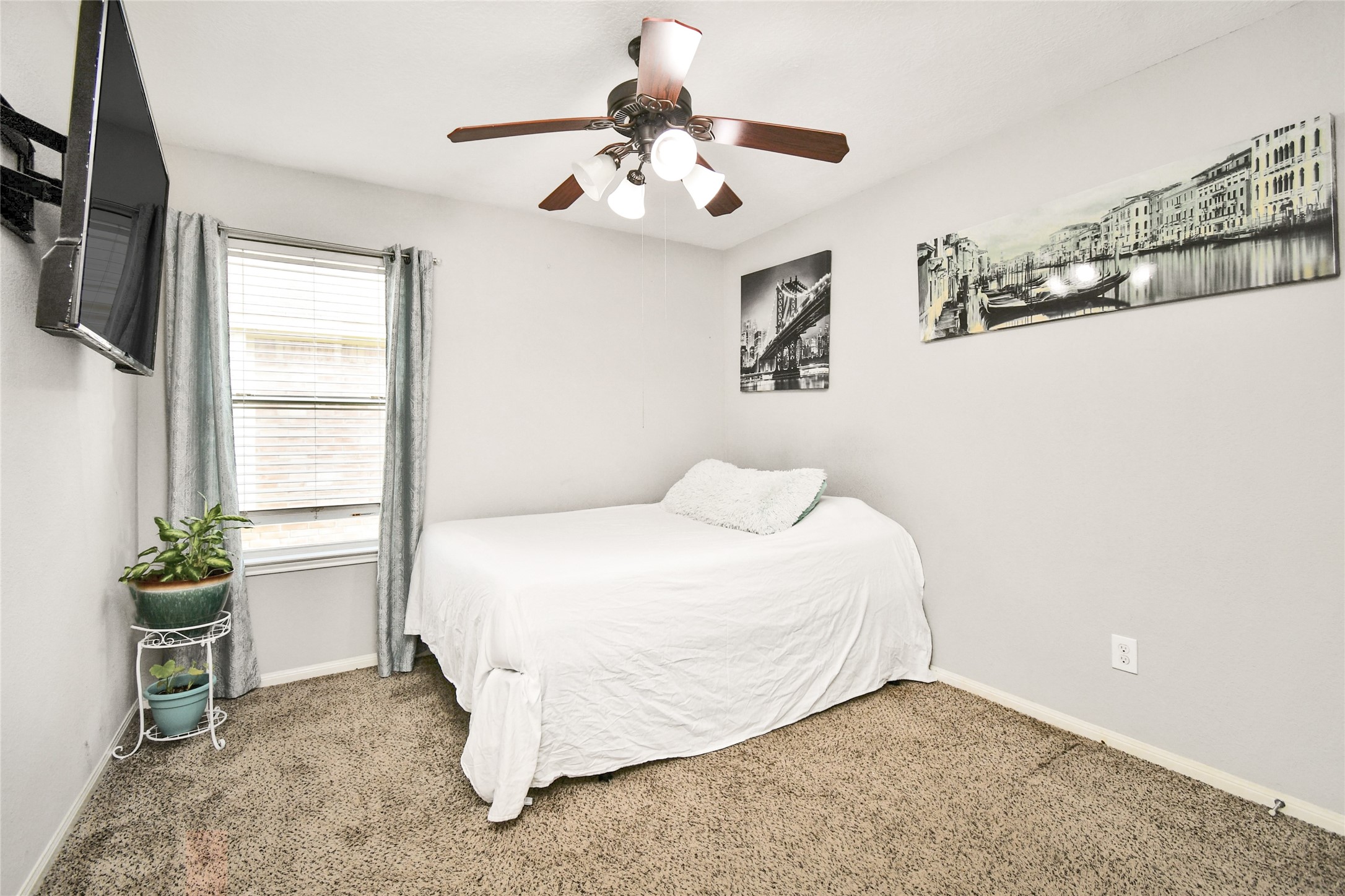 Comfortable secondary bedroom with mounted TV, ceiling fan, and soft carpet flooring