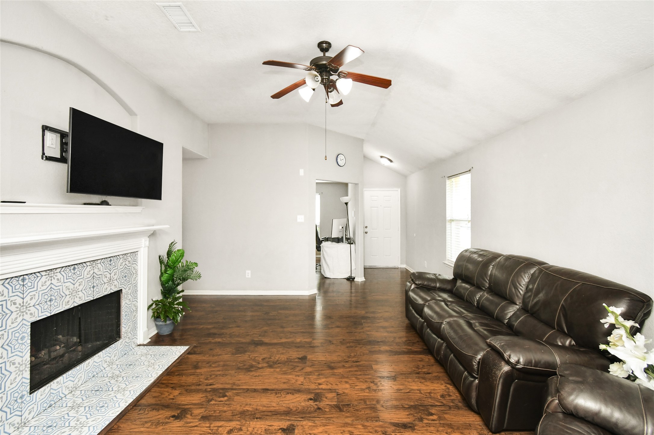 Bright open living room with a cozy fireplace, ceiling fan, and easy flow into the kitchen and front entry.