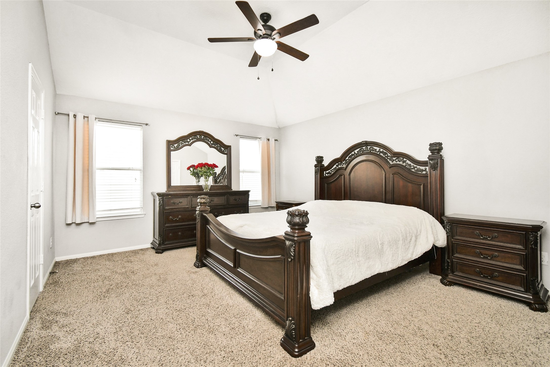 Spacious primary bedroom featuring vaulted ceilings, a ceiling fan, and plenty of natural light from dual windows.
