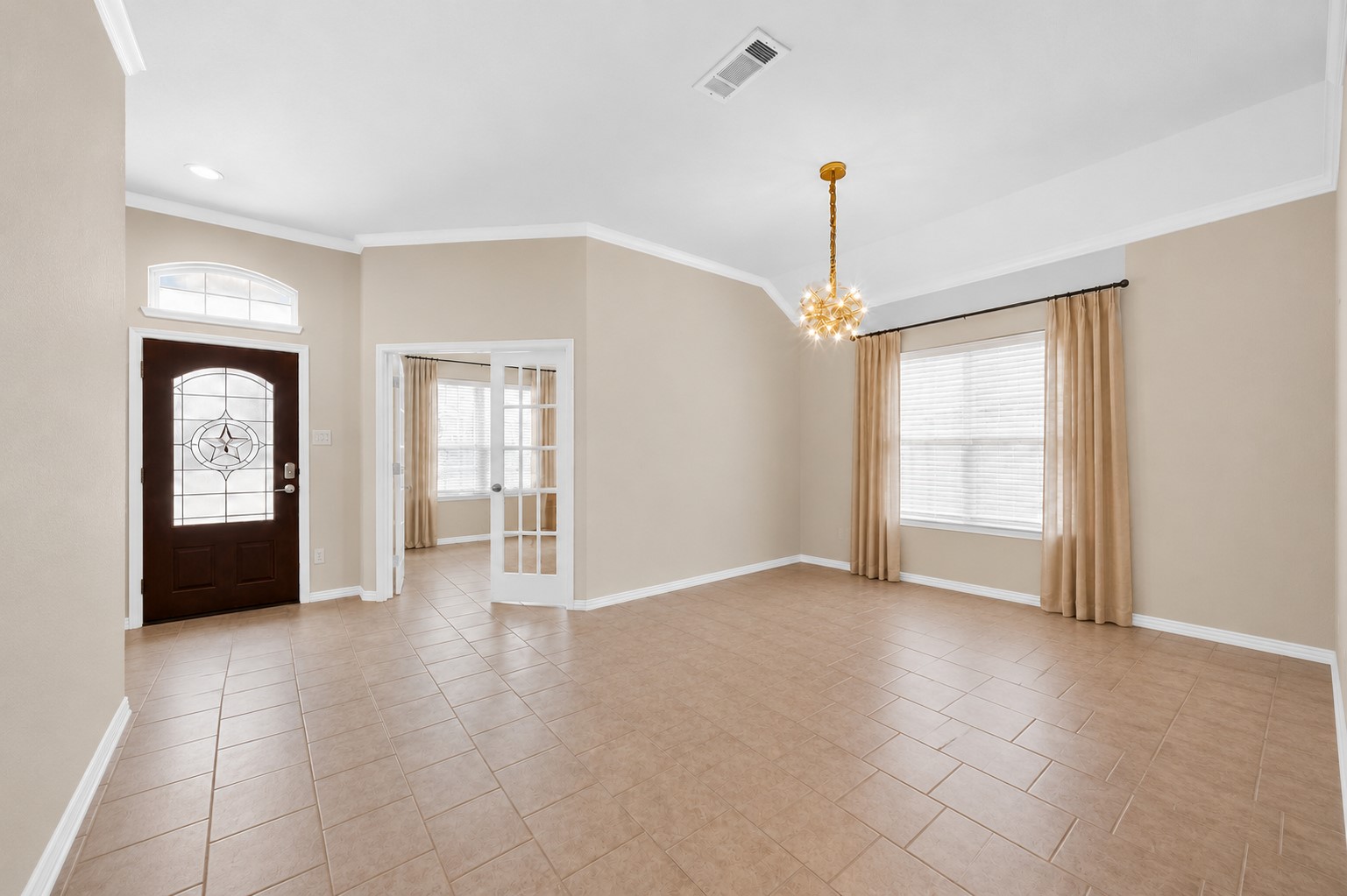 Furniture and personal dcor have been digitally removed to showcase the dining rooms layout, tile flooring, crown molding, and natural light. French doors connect to an adjacent room near the front entry. Furniture and personal dcor have been digitally removed to showcase the dining rooms layout, tile flooring, crown molding, and natural light. French doors connect to an adjacent room near the front entry.