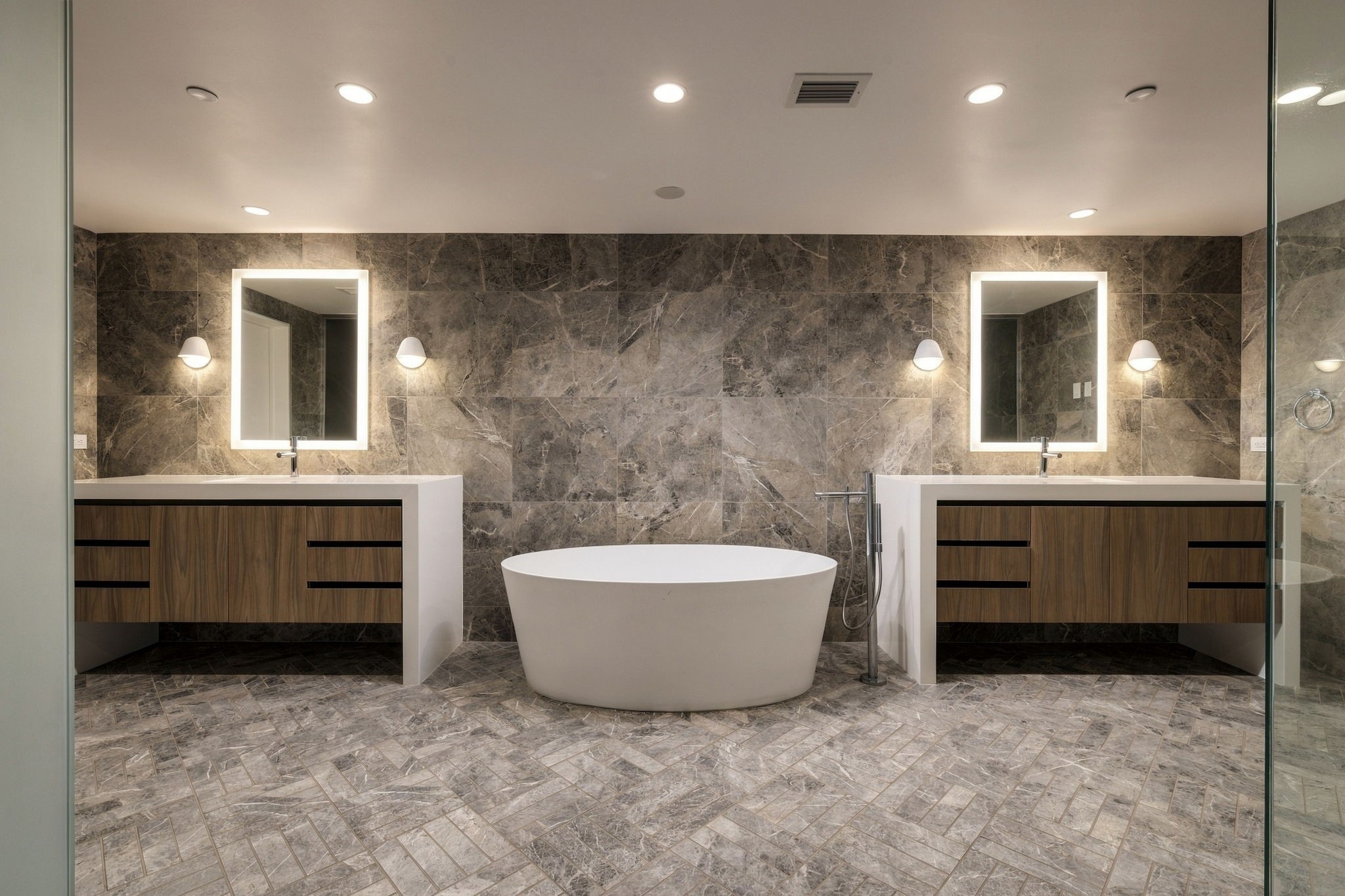 Inside the main-floor primary en suite bathroom, two wood vanities with waterfall quartz countertops and Robern medicine cabinets flank a freestanding Barclay soaking tub.