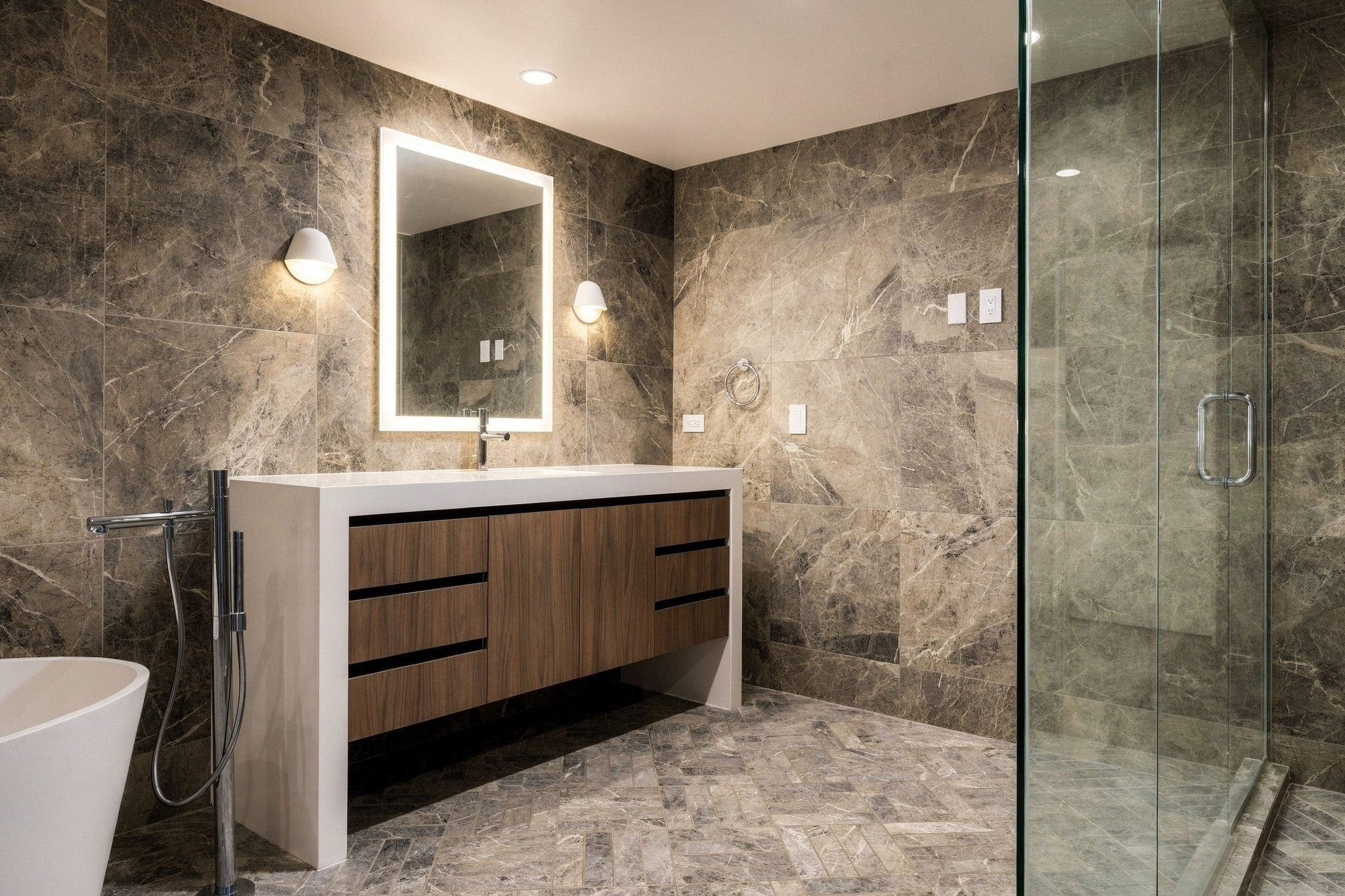 A shower, private water closet and floor-to-ceiling gray marble tile create an extraordinary spa experience in the main-floor primary en suite bathroom.