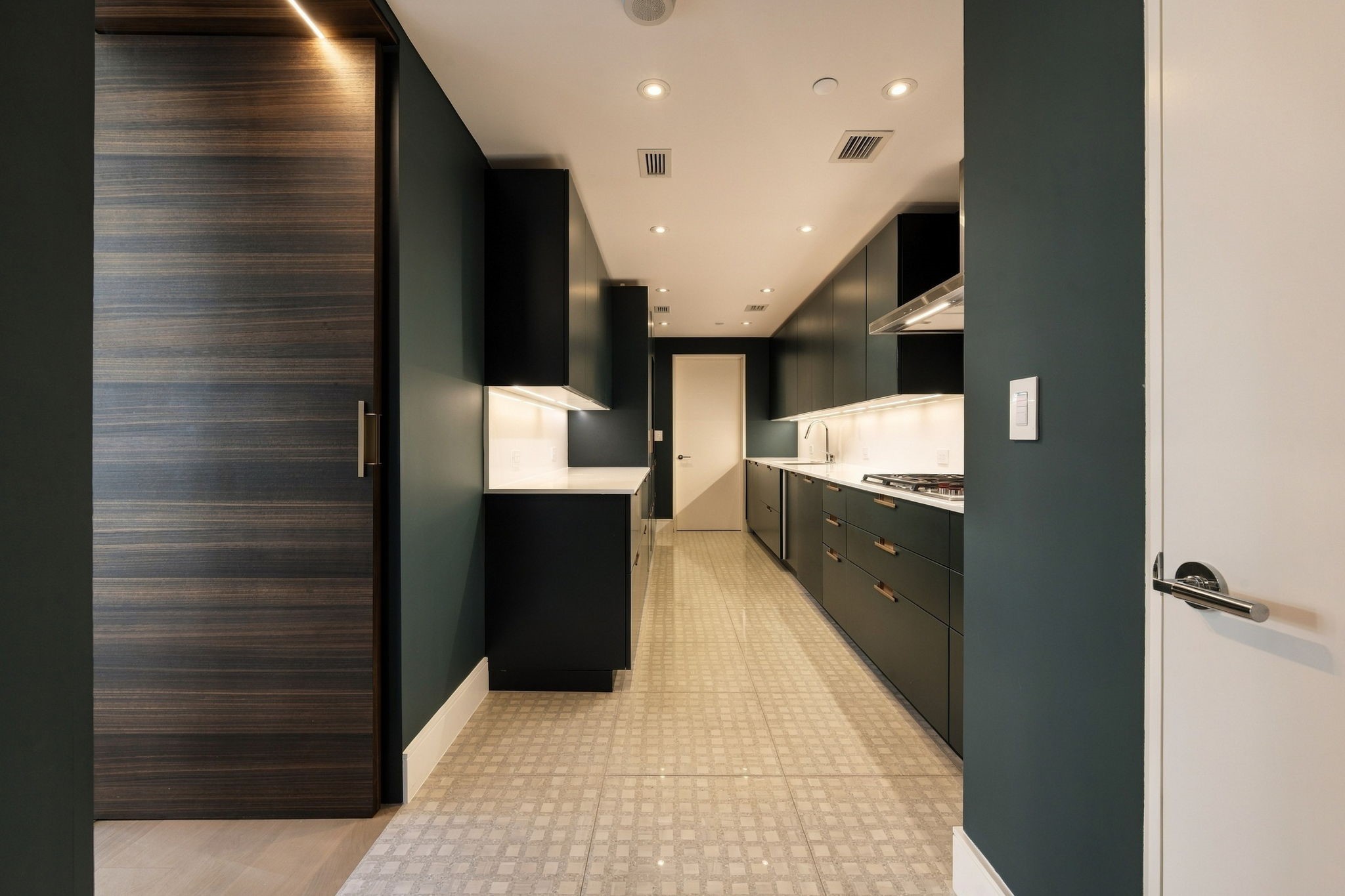 A concealed door reveals the working kitchen and storage pantry, where crisp white quartz counters show off emerald-green Cesar cabinetry. A Wolf cooktop, oven and microwave, Asko dishwasher, and Sub-Zero freezer and wine refrigerator complete the functional space. Complete with fully custom built out pantry with adjustable lighting.
