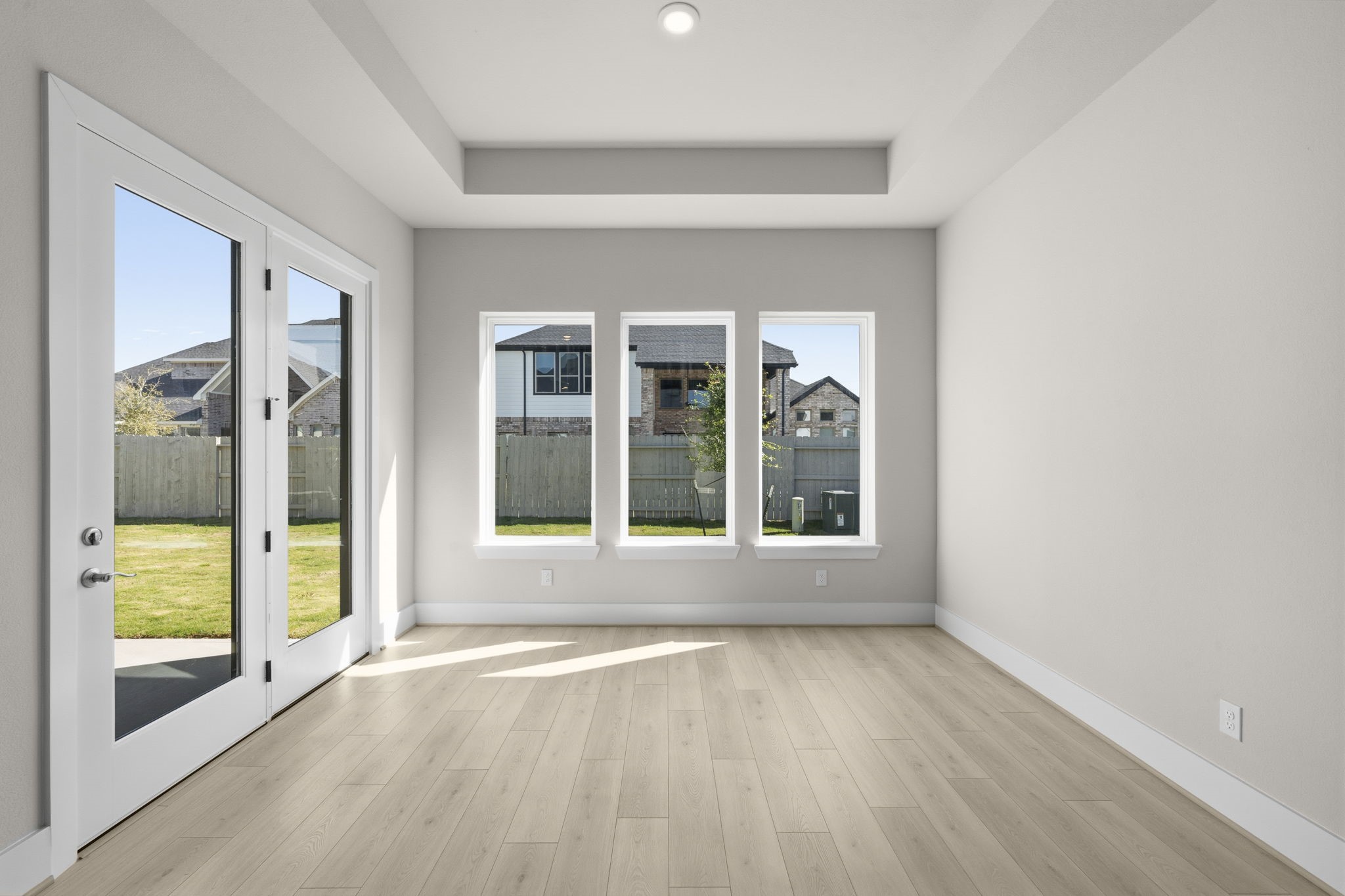 The sunroom comes with large windows and light wood flooring, offering a view of a fenced backyard. French doors provide access to the outdoor space, enhancing the open feel.