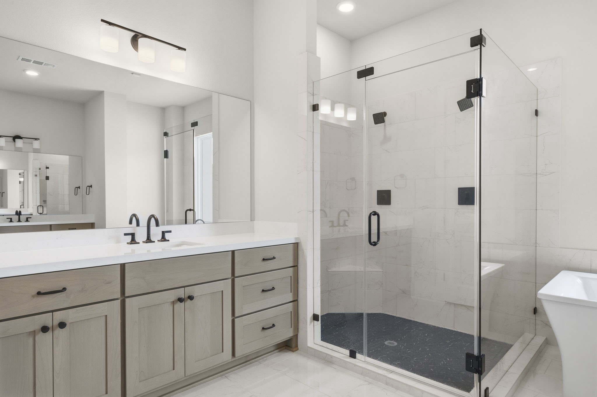 This primary bathroom features a spacious glass-enclosed shower, dual sinks with modern fixtures, light wood cabinetry, and bright lighting, creating a clean, contemporary, and home spa sanctuary