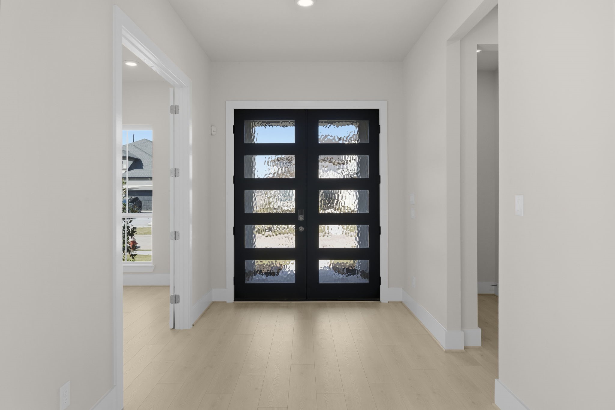 Striking black front door featuring glass panels. The hallway is bright, with light wood flooring and neutral walls, creating a welcoming and contemporary feel.