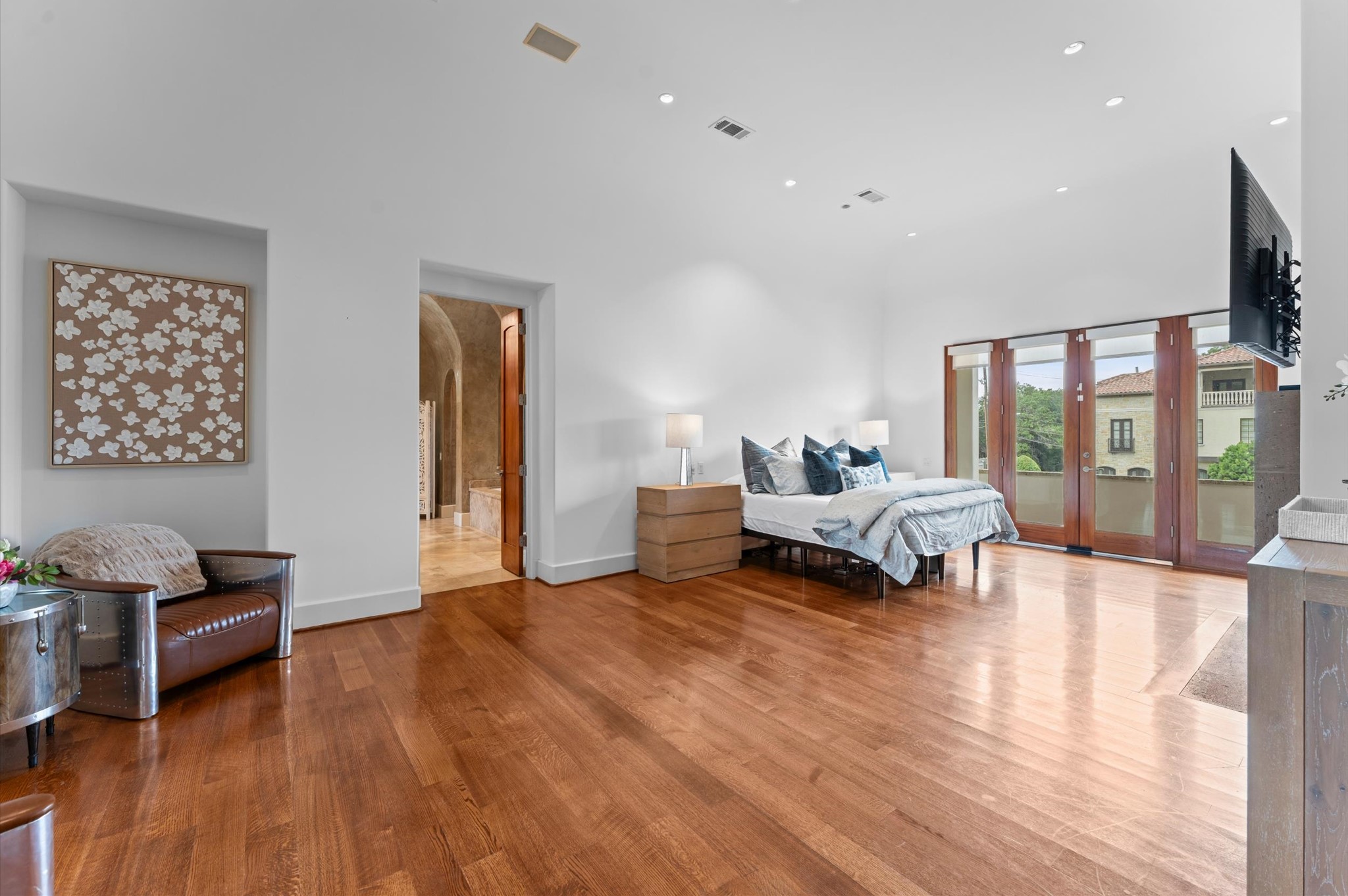 A spacious primary bedroom showcases rich mahogany flooring, a striking stone fireplace, and multiple private balconies overlooking the estate grounds.