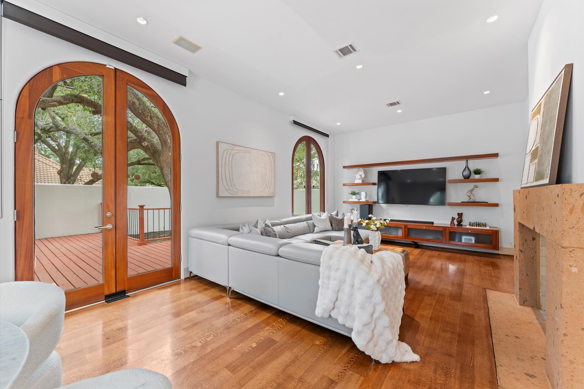 The rear living area features a striking double-sided fireplace, custom floating media and display cabinetry, and soaring proportions. Tall arched glass doors open to the covered loggia and elevated side deck, creating an elegant connection between refined interior living and outdoor entertaining.