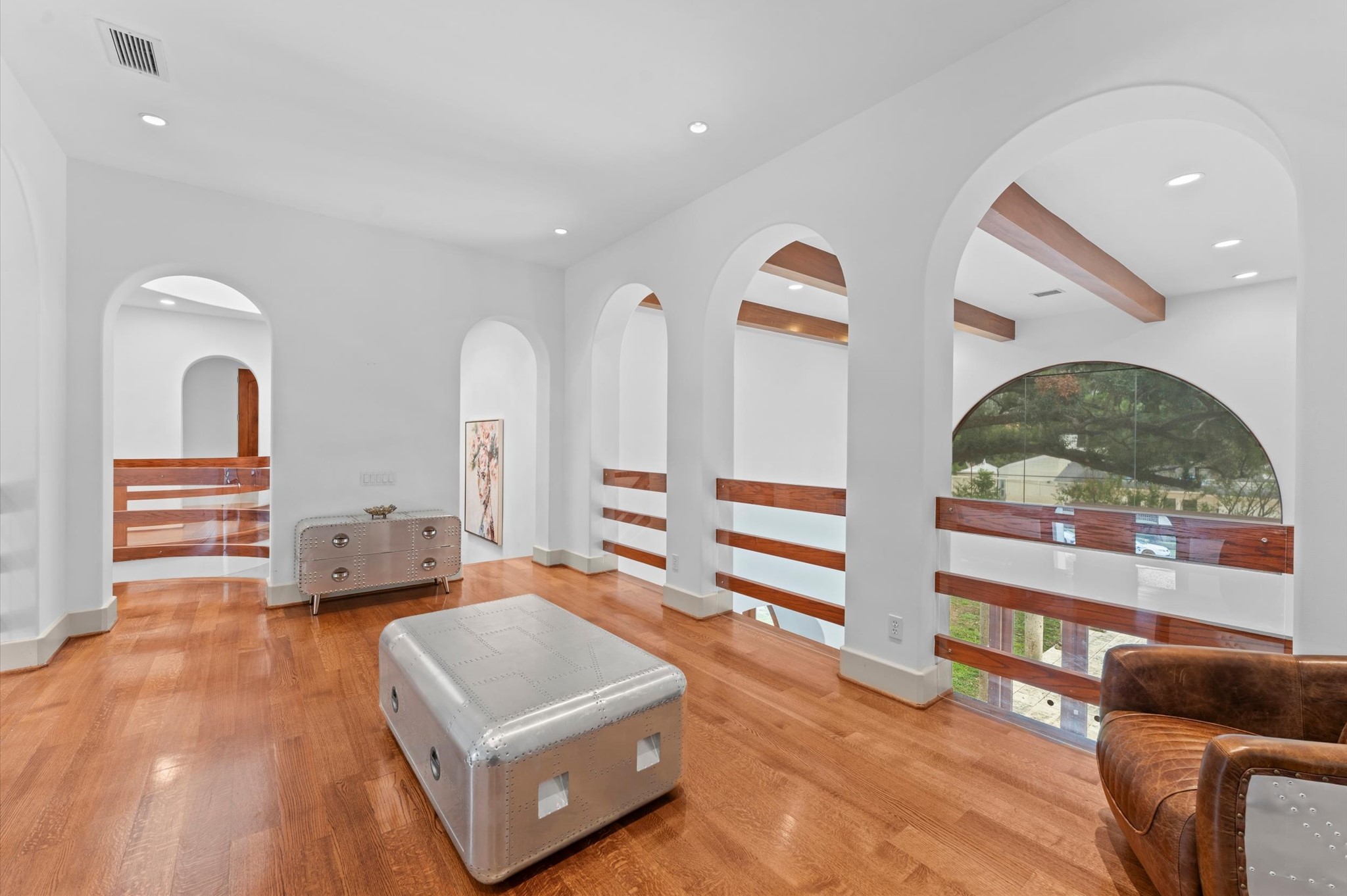 An elegant upper-level gallery featuring warm wood flooring, distinctive arched architectural openings, and custom wood-and-glass railings overlooking the home's dramatic interior.