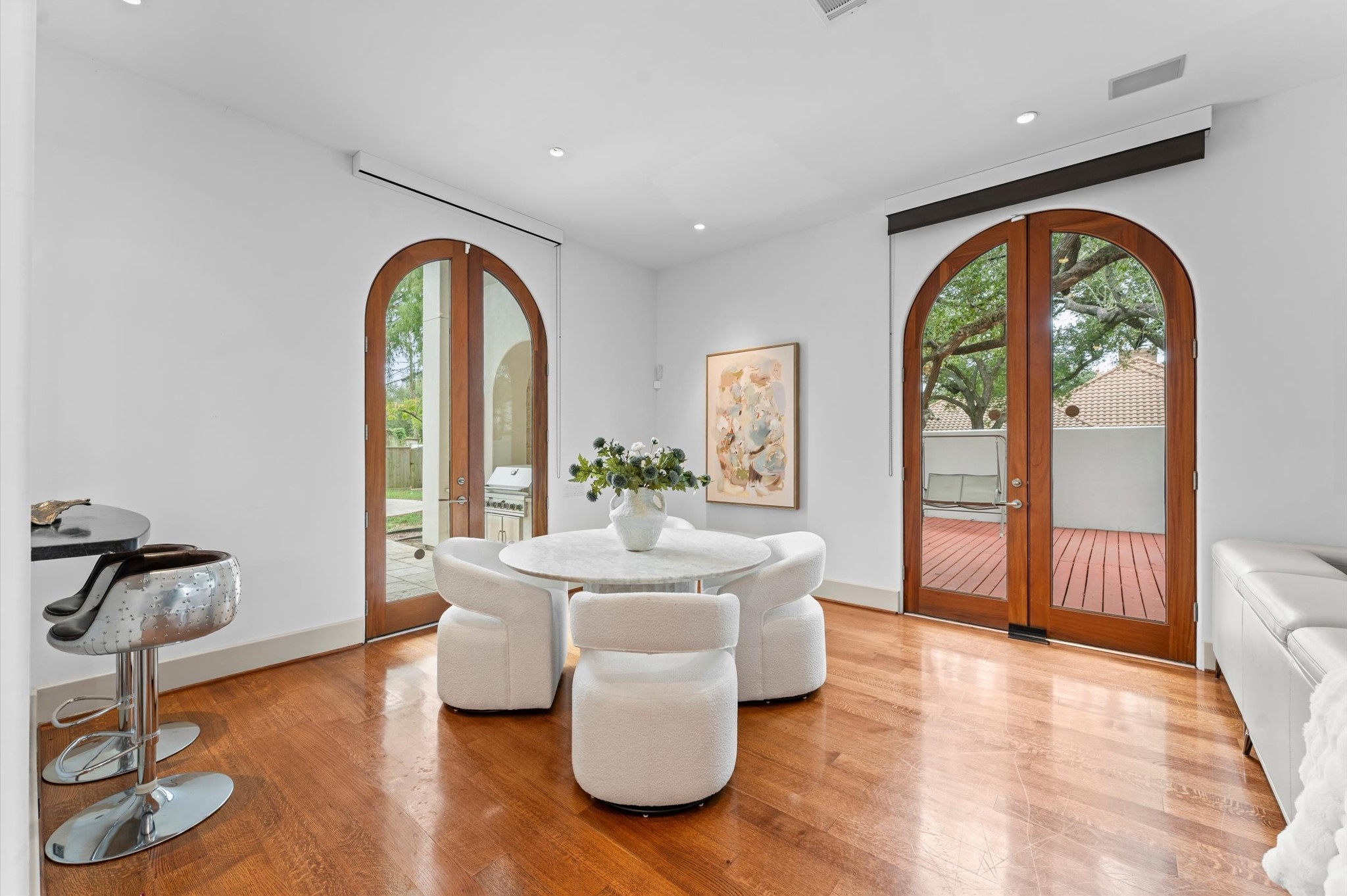 A light-filled gallery sitting area nestled beside the entertaining bar, featuring elegant arched mahogany doors that open to the outdoor patio. An inviting setting for morning coffee, intimate conversation, or effortless entertaining, with seamless indoor-outdoor flow.