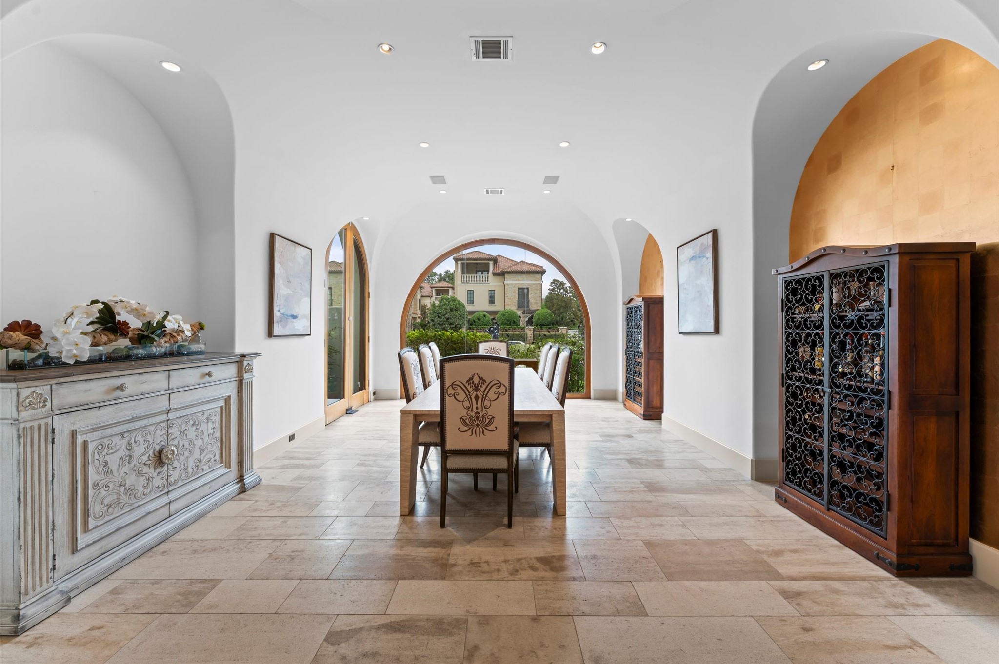 An elegant formal dining room distinguished by floor-to-ceiling arched windows, abundant natural light, imported travertine flooring, mahogany baseboards, recessed lighting, and exquisite gold-leaf accent walls.
