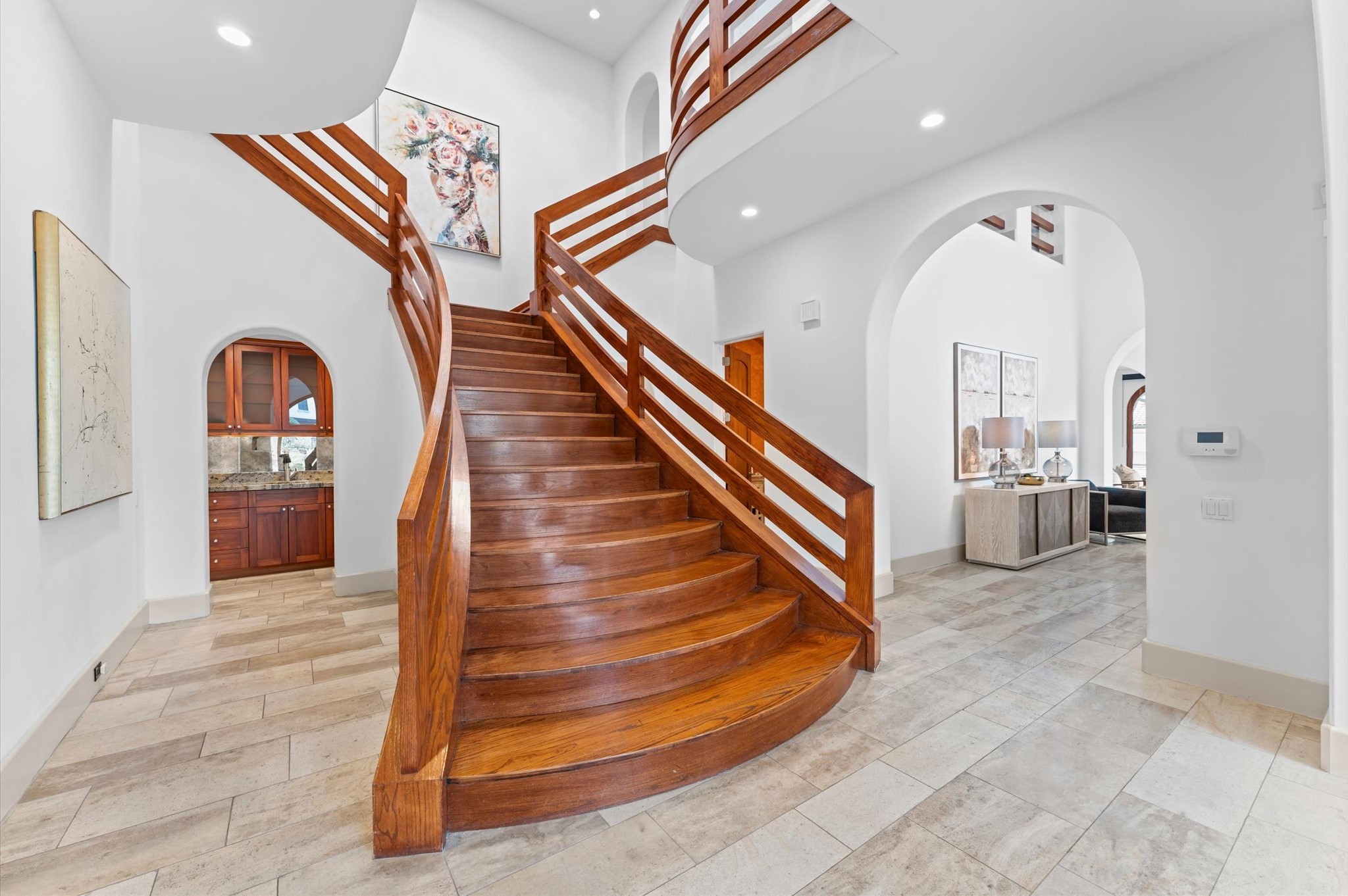 A striking bifurcated mahogany staircase rises from the double-height reception gallery, branching toward the upper gallery and connecting the private primary suite and secondary bedroom wings.