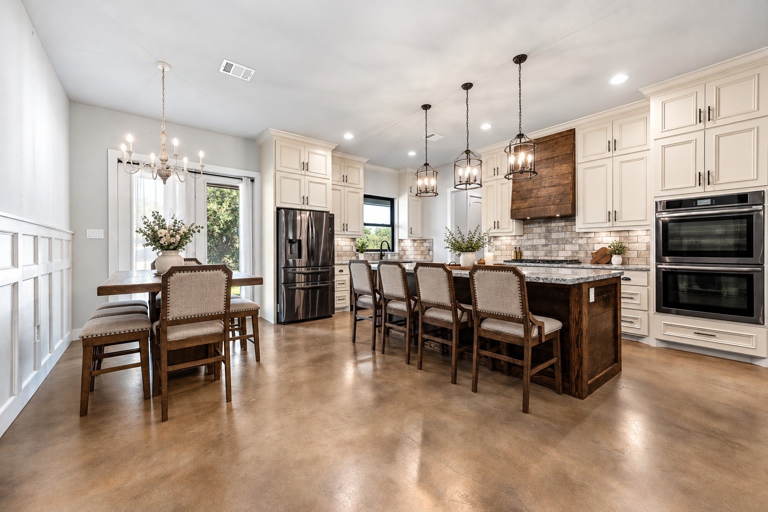 Dining area open to the kitchen, with wainscoting, pendant lighting, granite island and double wall ovens. This photo may be edited using AI tools.