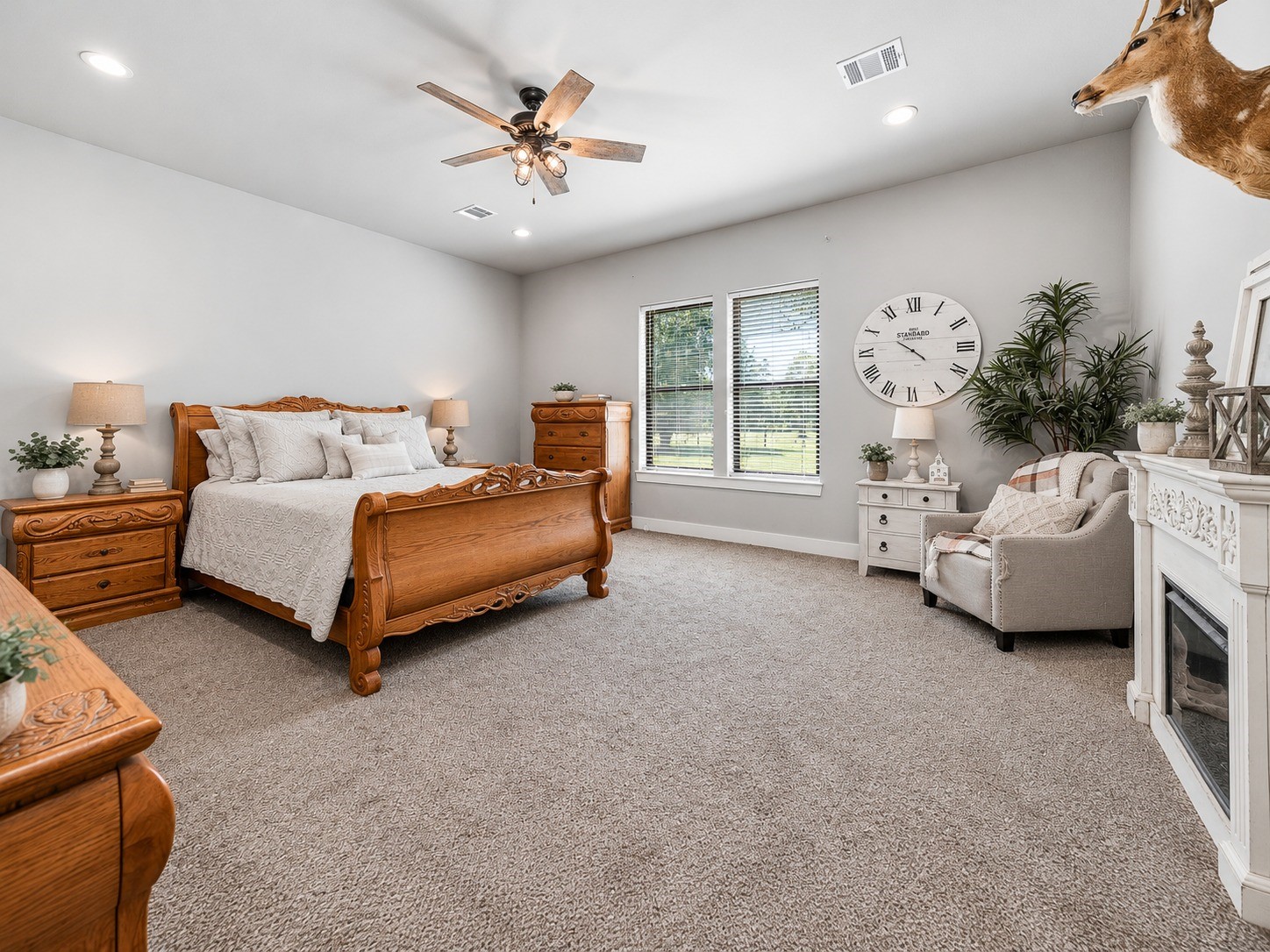 Spacious primary bedroom with carpet, ceiling fan and large windows overlooking the property. This photo may be edited using AI tools.