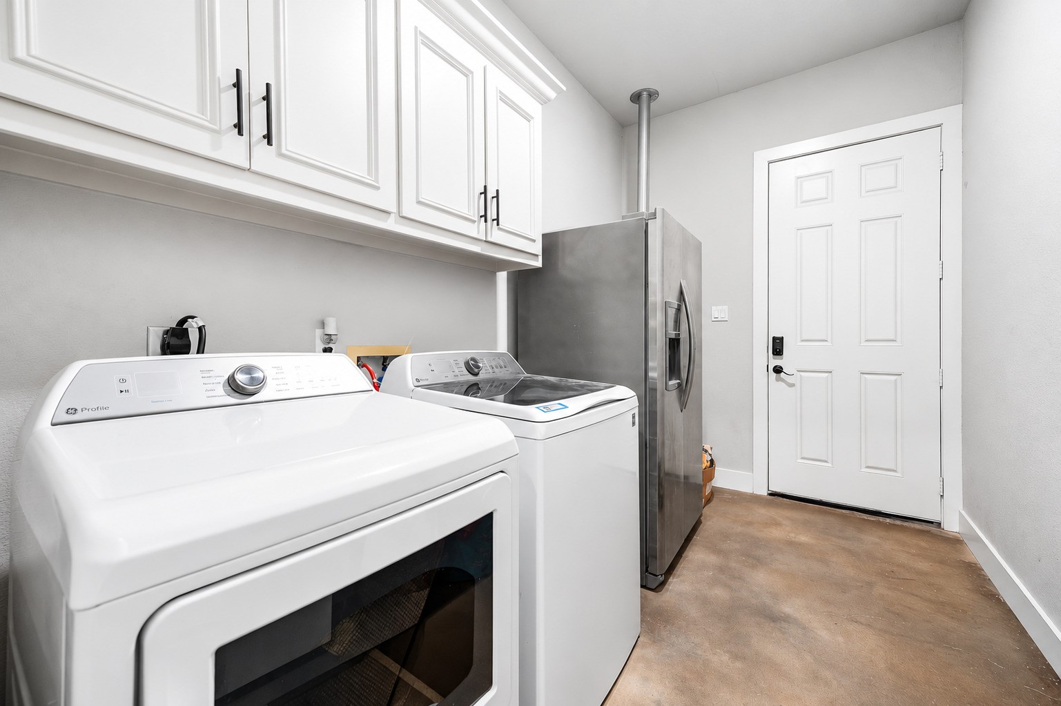 Laundry room with upper cabinets and space for a full-size washer and dryer. This photo may be edited using AI tools.