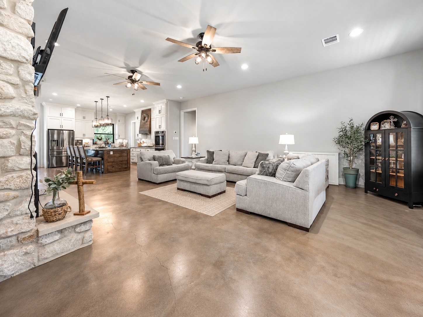 Open-concept family room with a stone fireplace, flowing into the kitchen and dining area. This photo may be edited using AI tools.