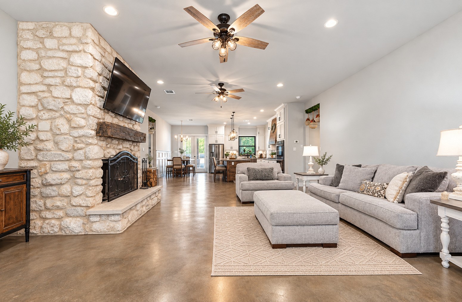 Family room with 10-ft ceilings, stained concrete floors and a floor-to-ceiling stone fireplace. This photo may be edited using AI tools.