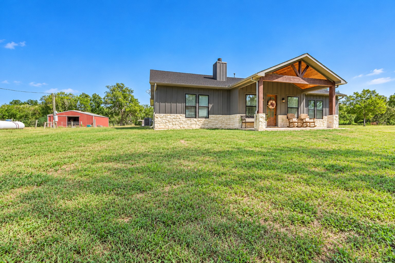 Side exterior of the home with board-and-batten siding and stone accents, with the red barn visible on the left. This photo may be edited using AI tools.