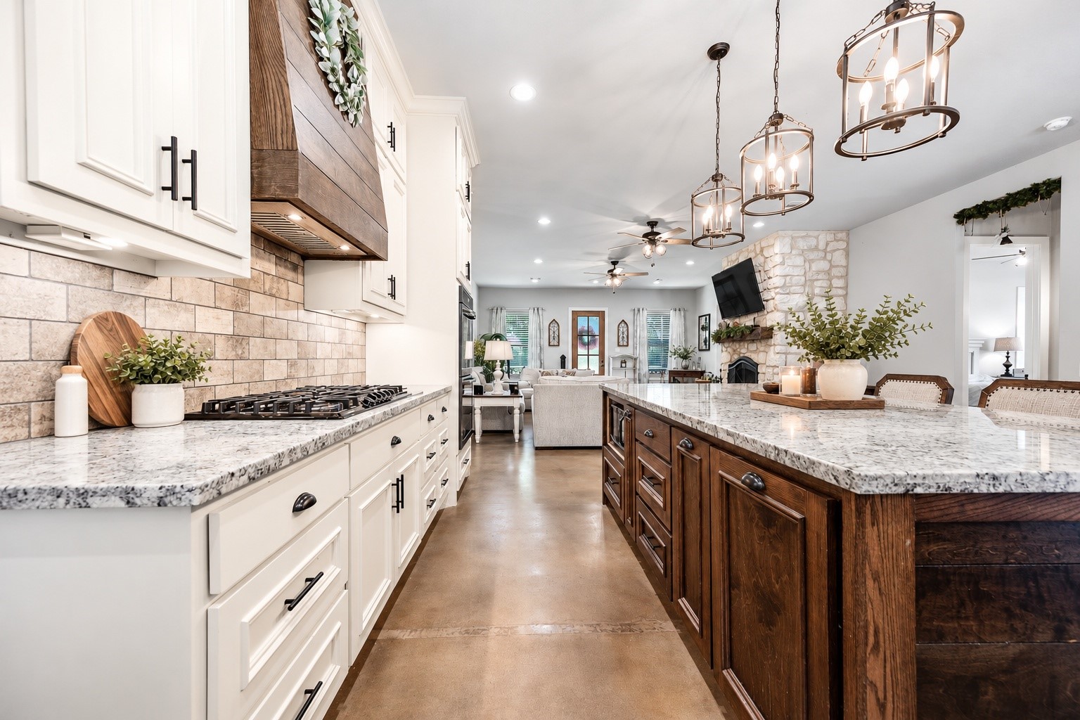 Kitchen with white custom cabinetry, granite countertops, stone-look backsplash, wood range hood and a large stained wood island. This photo may be edited using AI tools.