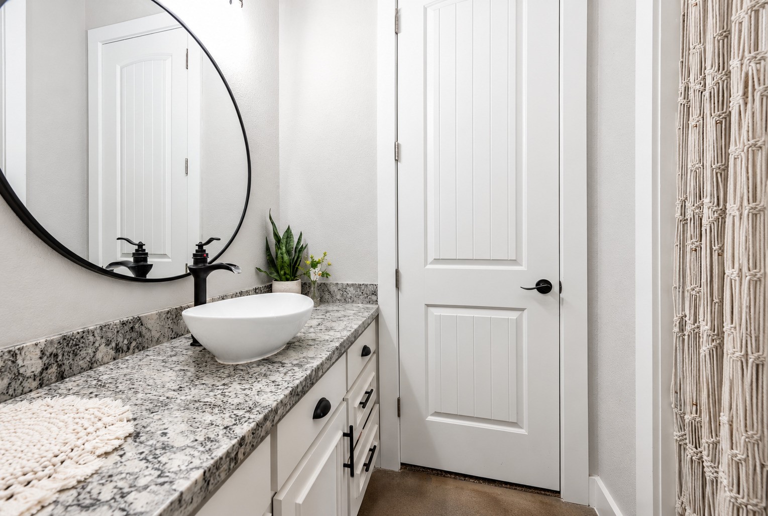 Bathroom with vessel sink, granite vanity and round mirror. This photo may be edited using AI tools.