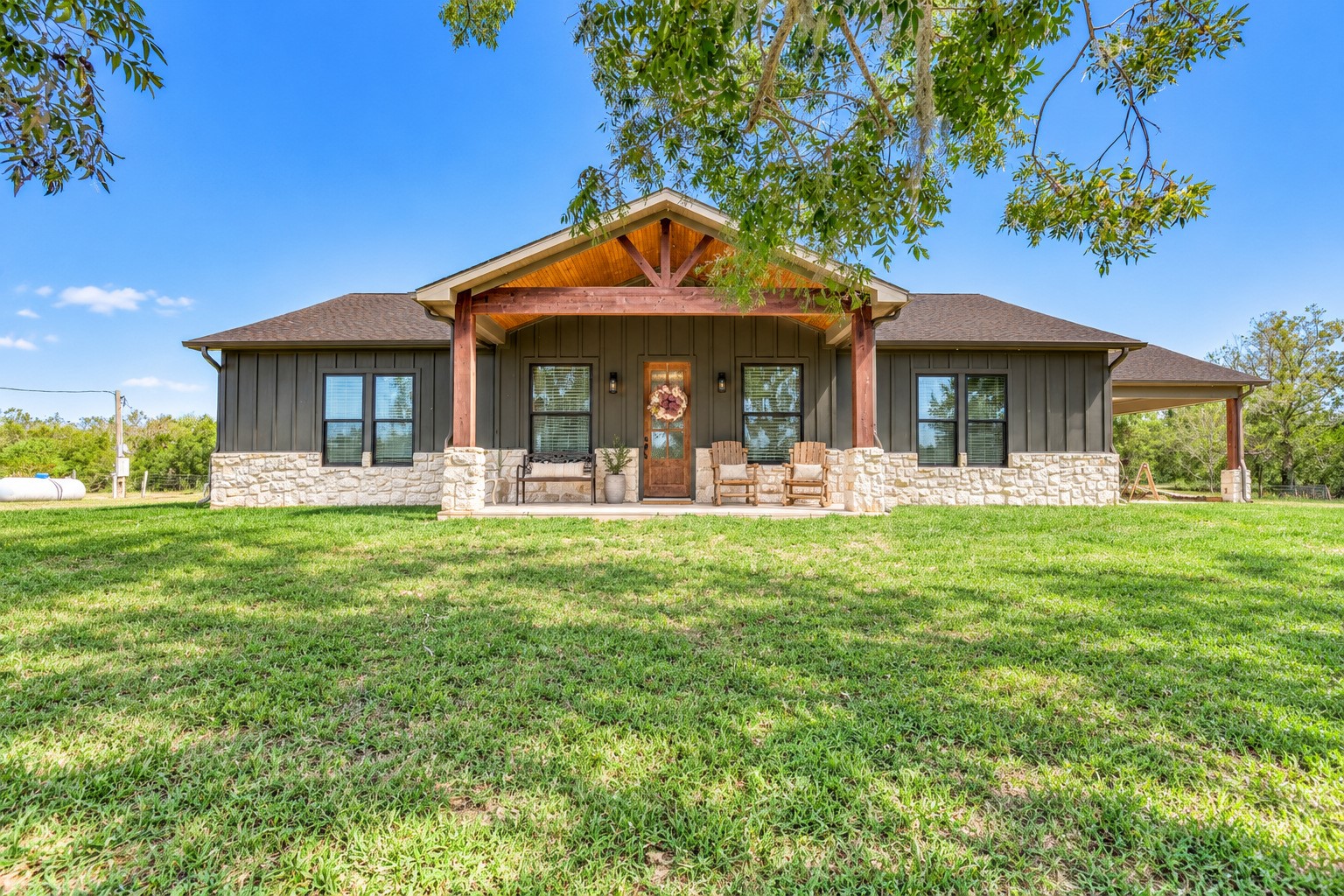Front exterior of this 2022-built country home on 15.9 acres in Sweeny, TX, with board-and-batten siding, stone wainscot and a covered front porch. This photo may be edited using AI tools.