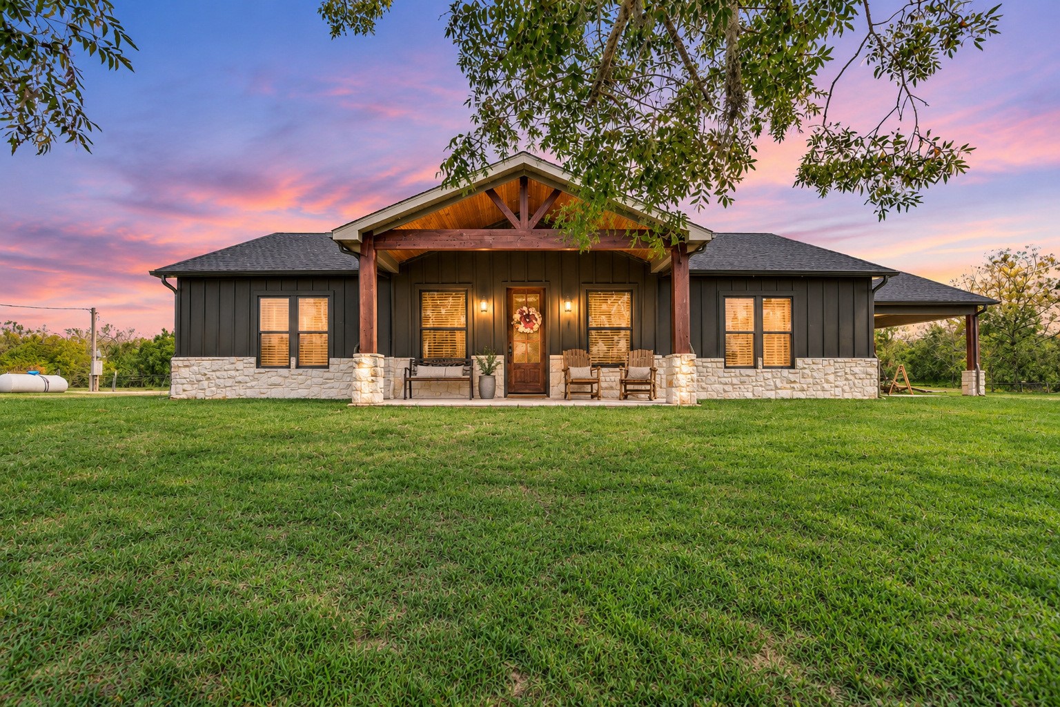 Front exterior at dusk of this 2022-built Sweeny, TX country home on 15.9 acres, with a covered front porch and board-and-batten siding. This photo may be edited using AI tools.