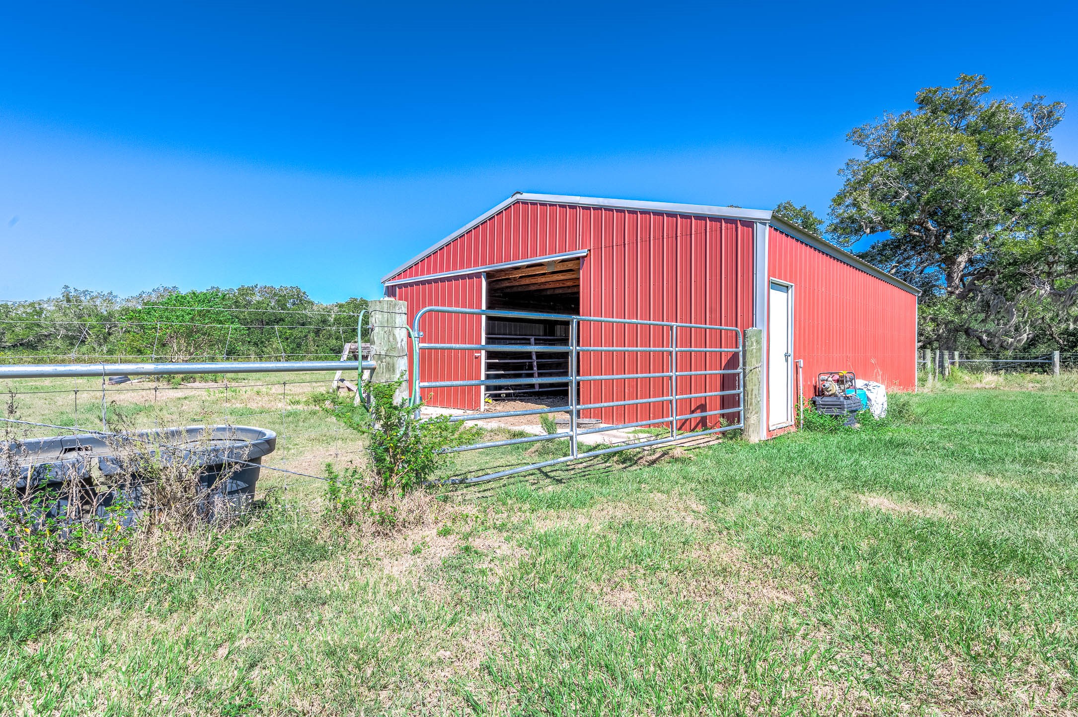 Red metal barn on the property, ready to be finished with stalls in the sizes of your choice. This photo may be edited using AI tools.