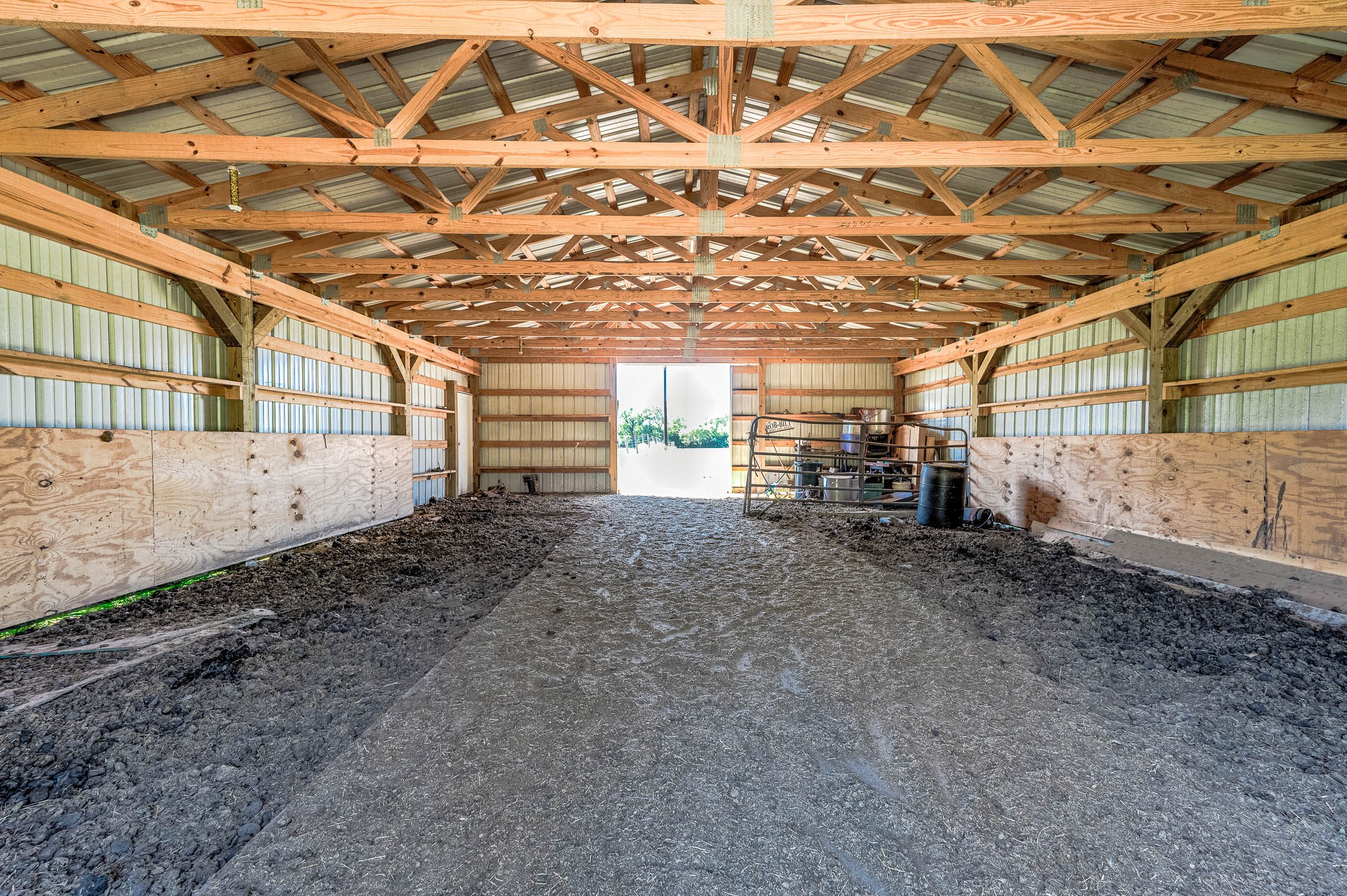 Barn interior with open center aisle, ready for stalls, tack or equipment storage. This photo may be edited using AI tools.