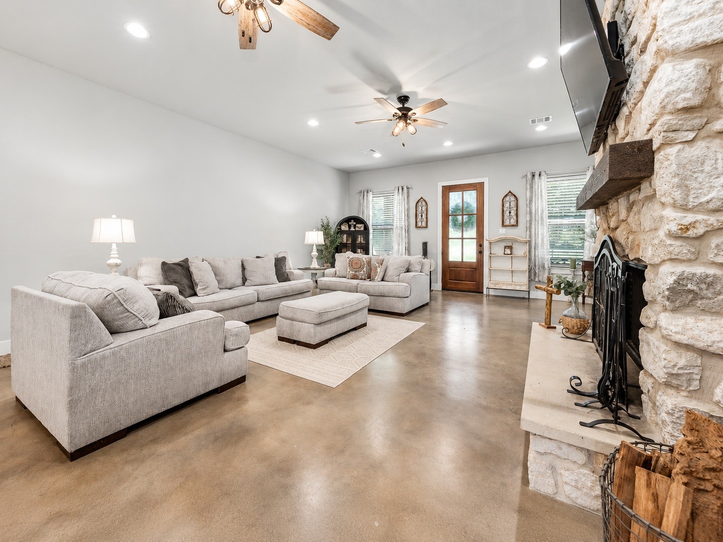 Open family room looking toward the front entry, with stained concrete floors, high ceilings and natural light. This photo may be edited using AI tools.