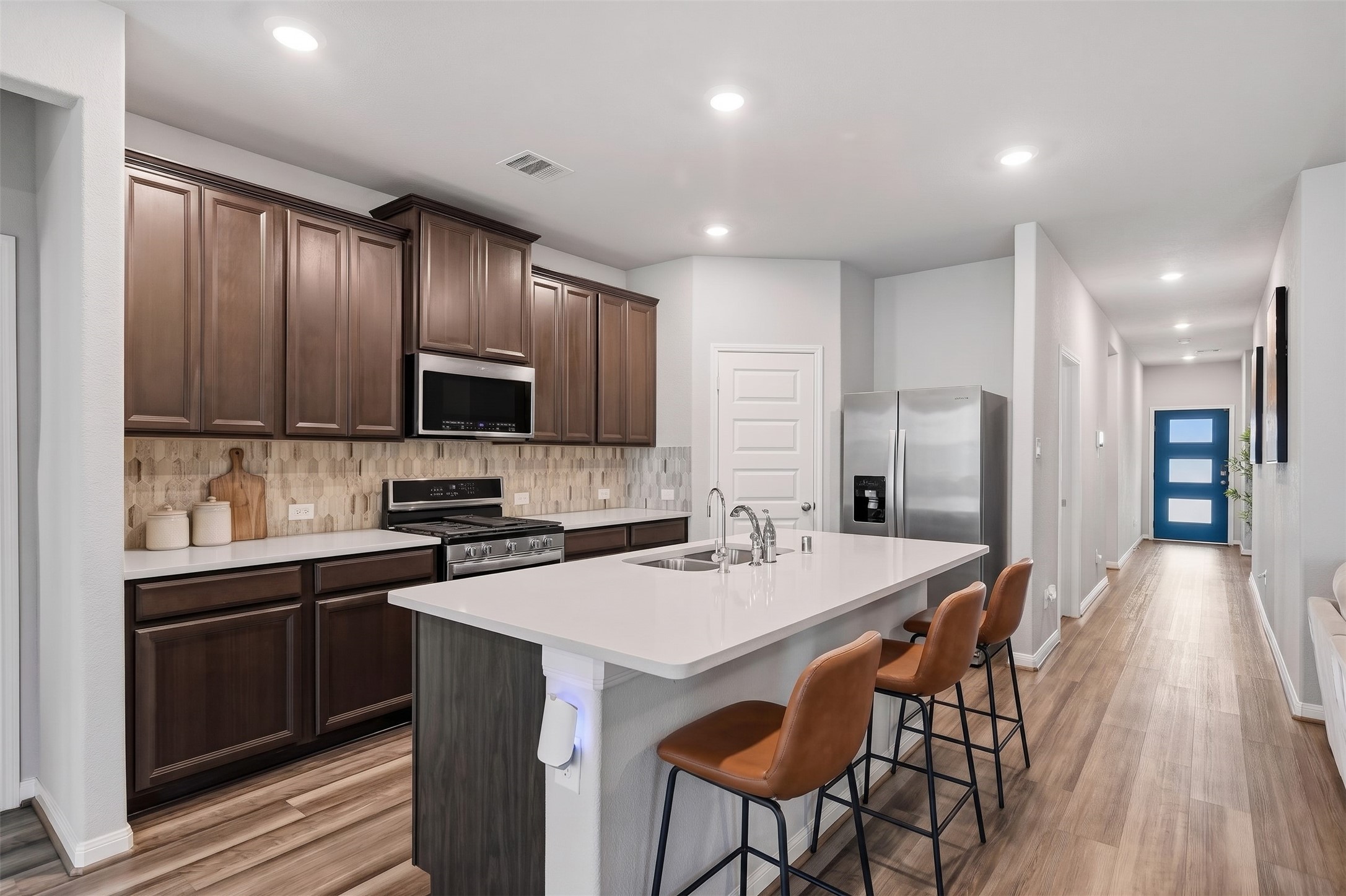 Virtually Staged: This spacious, modern kitchen features an open-concept layout with rich dark wood cabinetry, sleek white countertops, and an attractive tile backsplash. A large center island with an undermount double sink and breakfast bar provides generous counter space for meal preparation and casual dining. Stainless steel appliances complement the contemporary finishes, while recessed ceiling lighting brightens the entire space. Virtually Staged: This spacious, modern kitchen features an open-concept layout with rich dark wood cabinetry, sleek white countertops, and an attractive tile backsplash. A large center island with an undermount double sink and breakfast bar provides generous counter space for meal preparation and casual dining. Stainless steel appliances complement the contemporary finishes, while recessed ceiling lighting brightens the entire space.