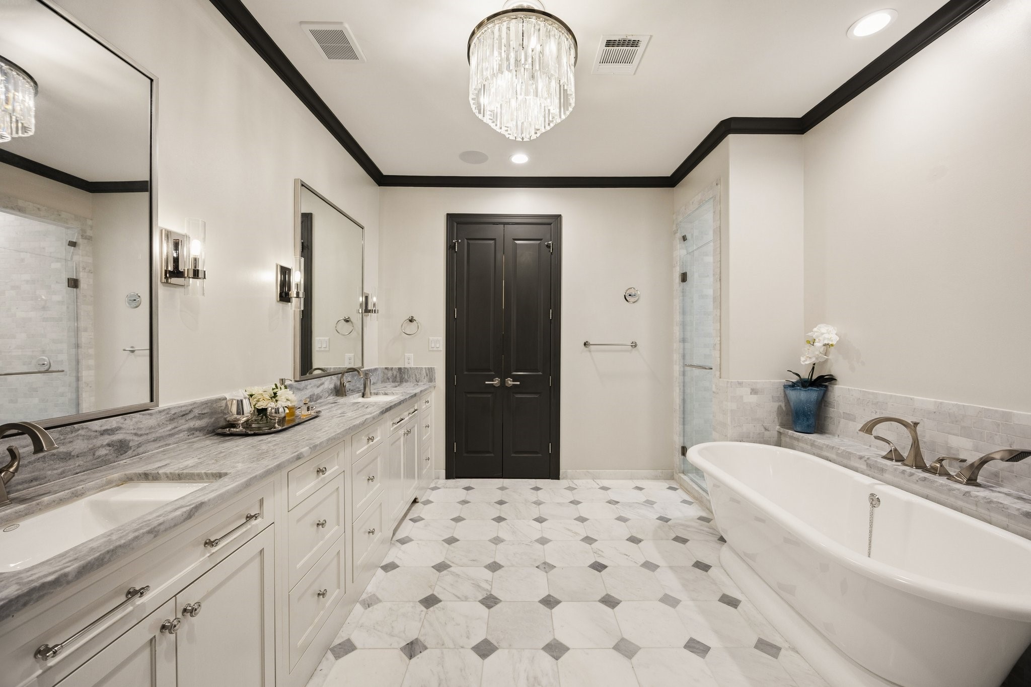 Luxurious primary bathroom featuring dual vanities, marble countertops, designer lighting, and two spacious walk-in closets with custom California Closets organization systems and built-ins.