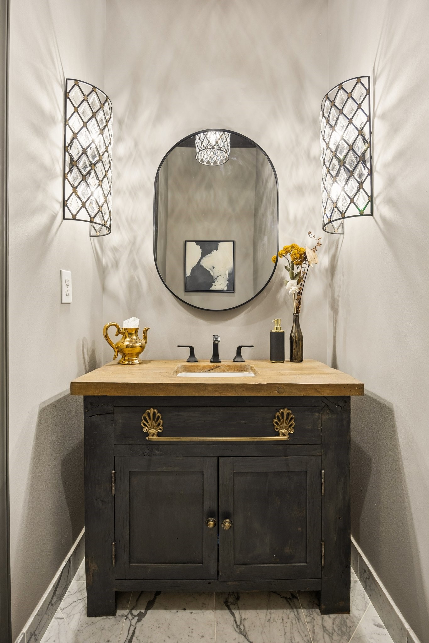 Elegant powder room featuring a custom vanity with natural stone countertop, decorative vessel sink, designer wall sconces, and a statement mirror.