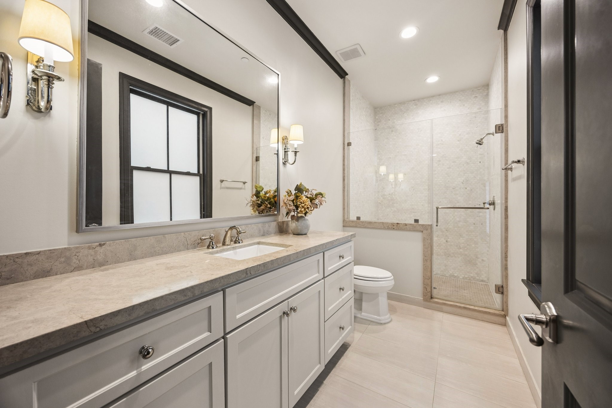 Elegant secondary bedroom en-suite bathroom featuring a spacious stone countertop vanity, custom cabinetry, and a beautifully tiled glass-enclosed walk-in shower.