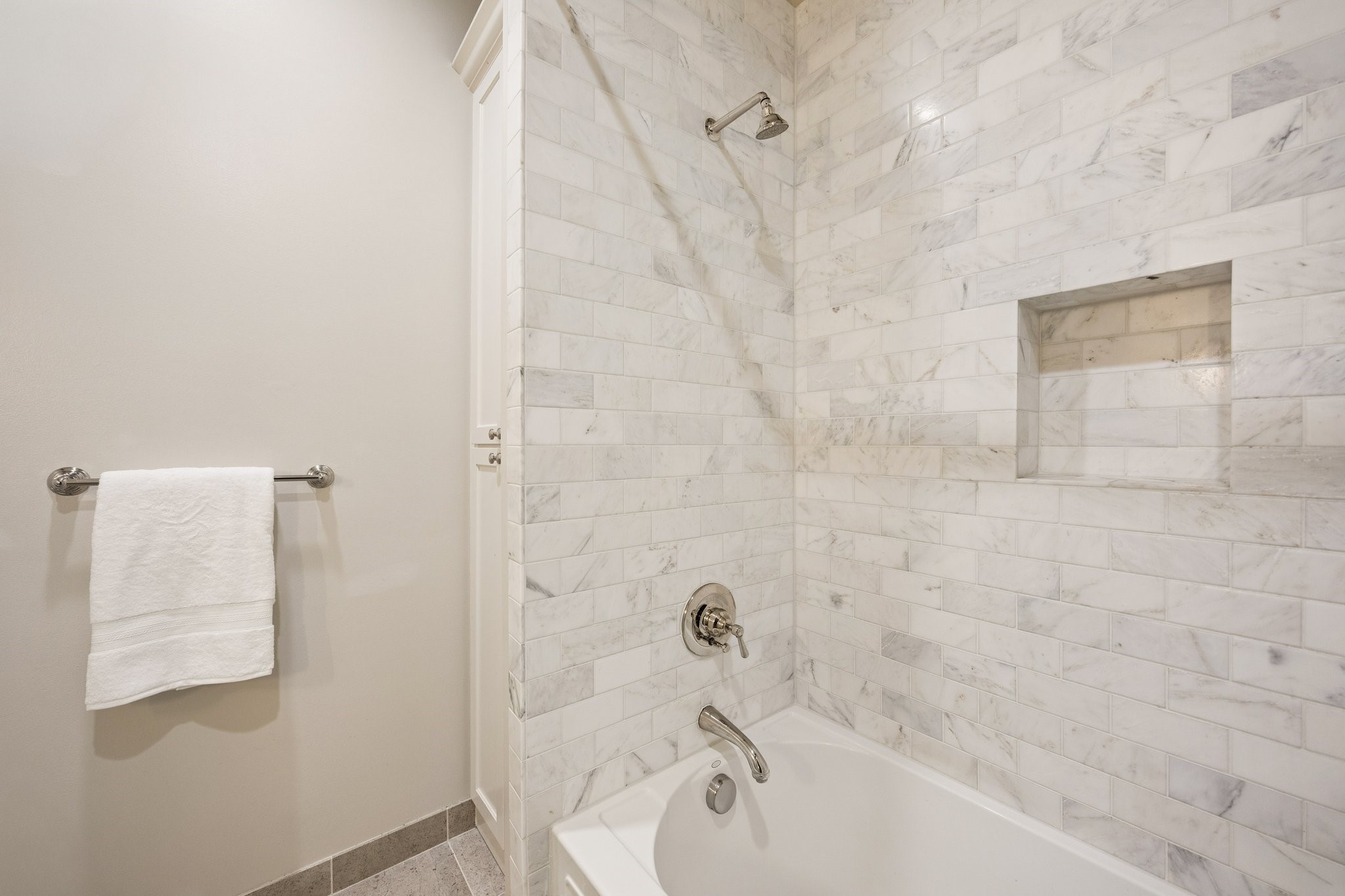 Beautifully tiled tub and shower combination in the first-floor en-suite bathroom, featuring elegant marble-look tile and a built-in shower niche.