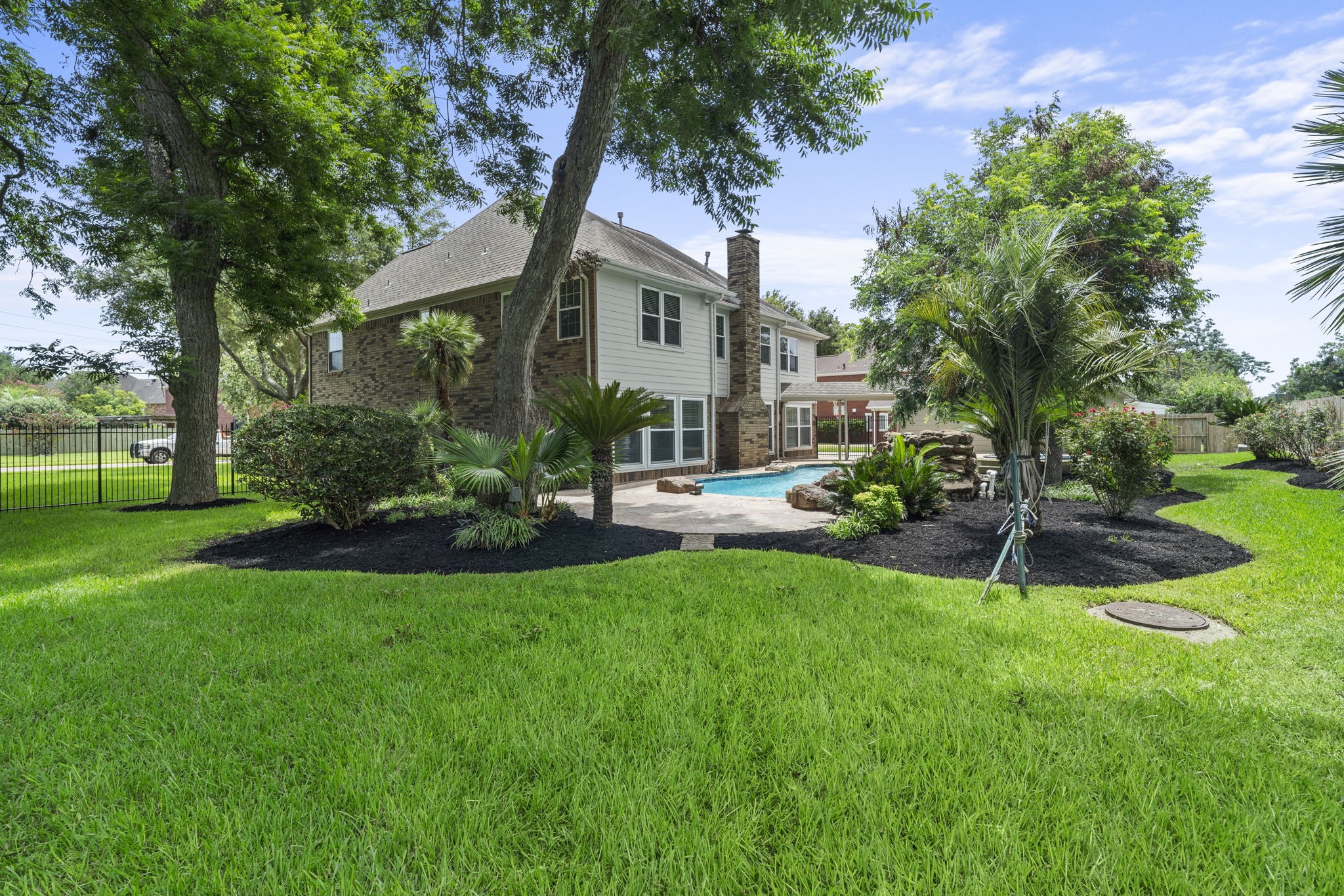 A beautifully landscaped backyard offers generous green space beyond the pool, with mature trees creating a picturesque setting for outdoor living.