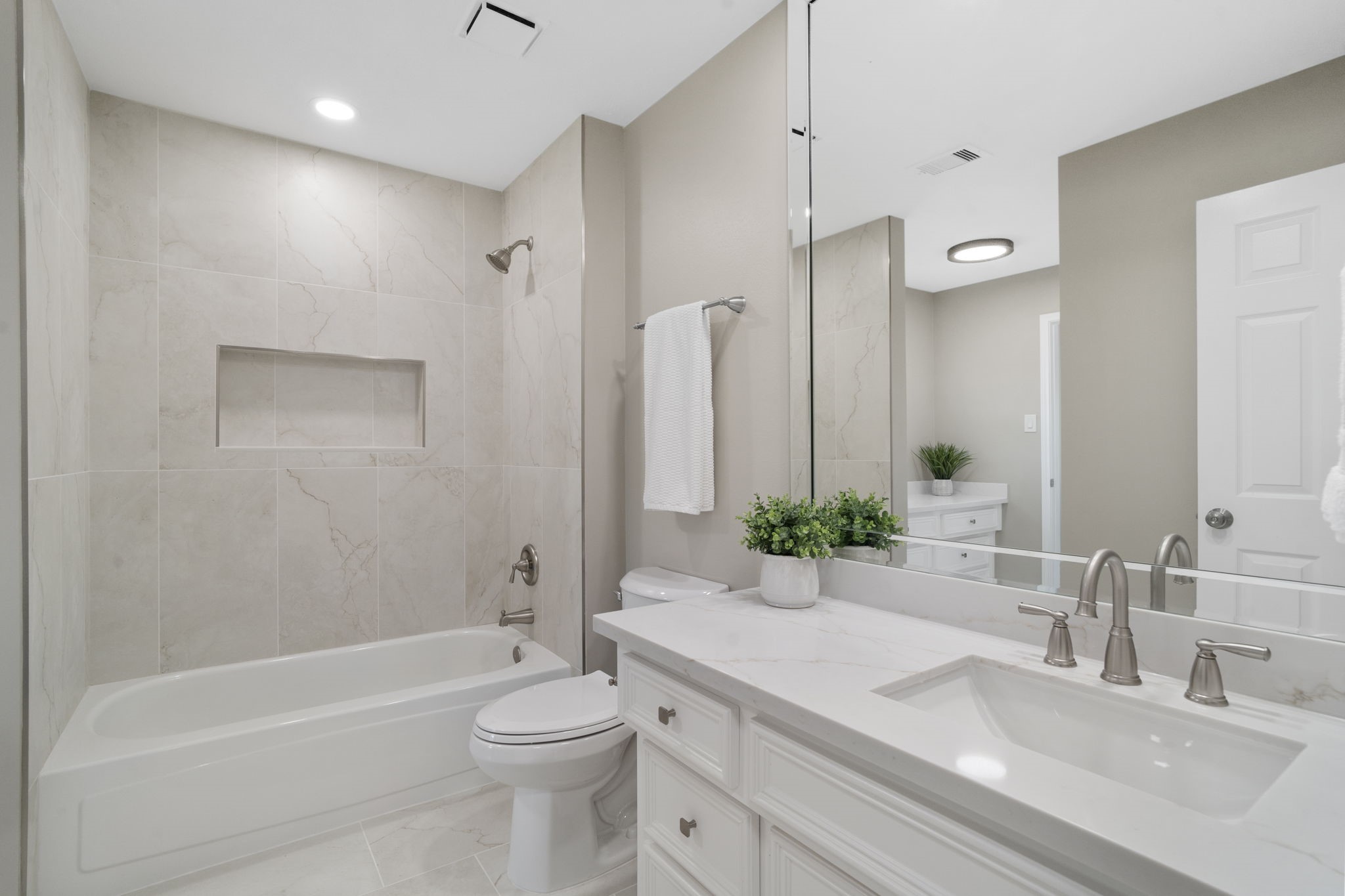This beautifully updated secondary en-suite bath offers convenient dual access from both the bedroom & hallway, with quartz countertops, abundant cabinetry & a tiled tub/shower surround with built-in niche.