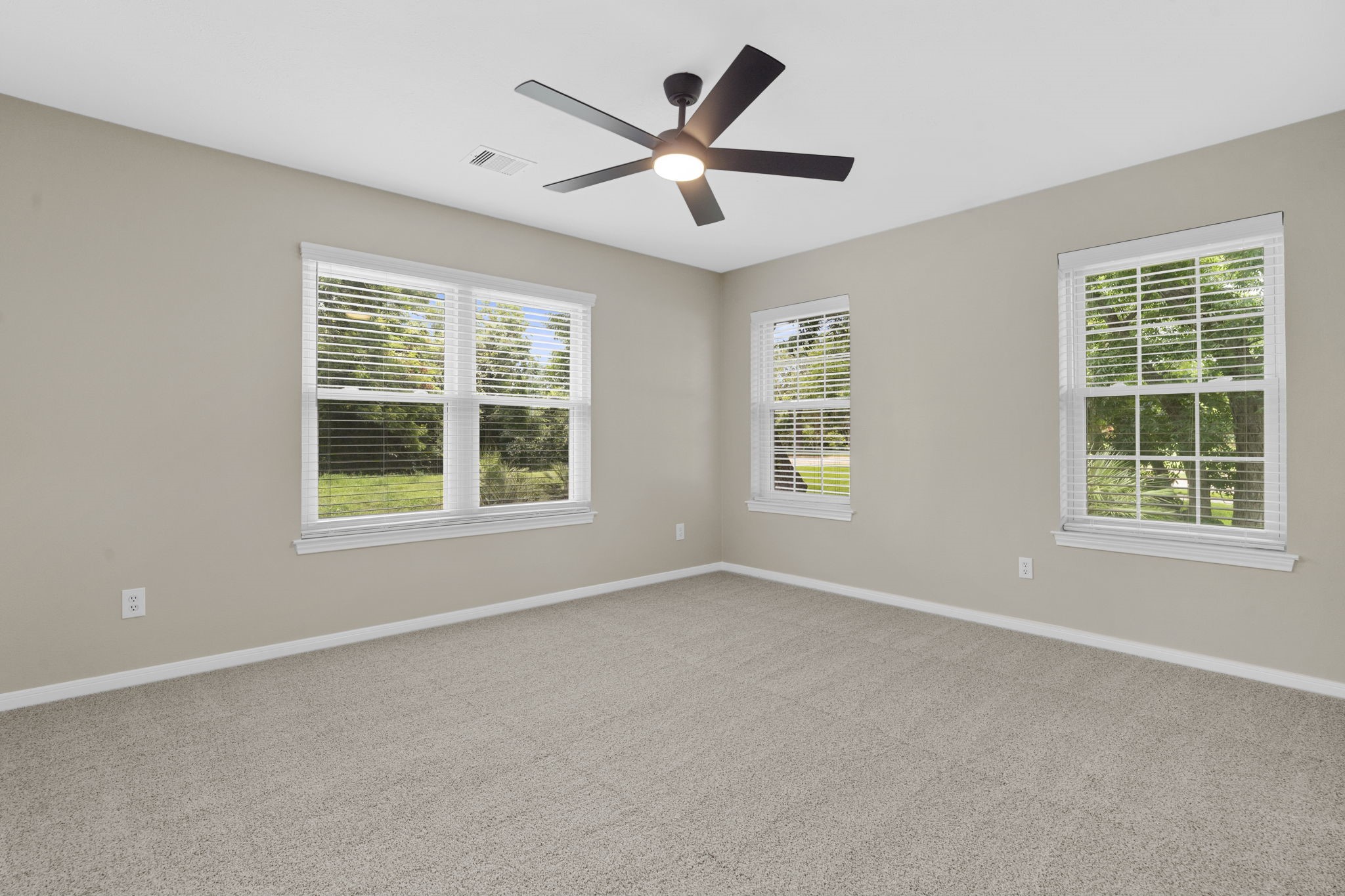 A spacious secondary bedroom is filled with natural light from multiple windows, offering ample room for a comfortable sitting area or workspace.