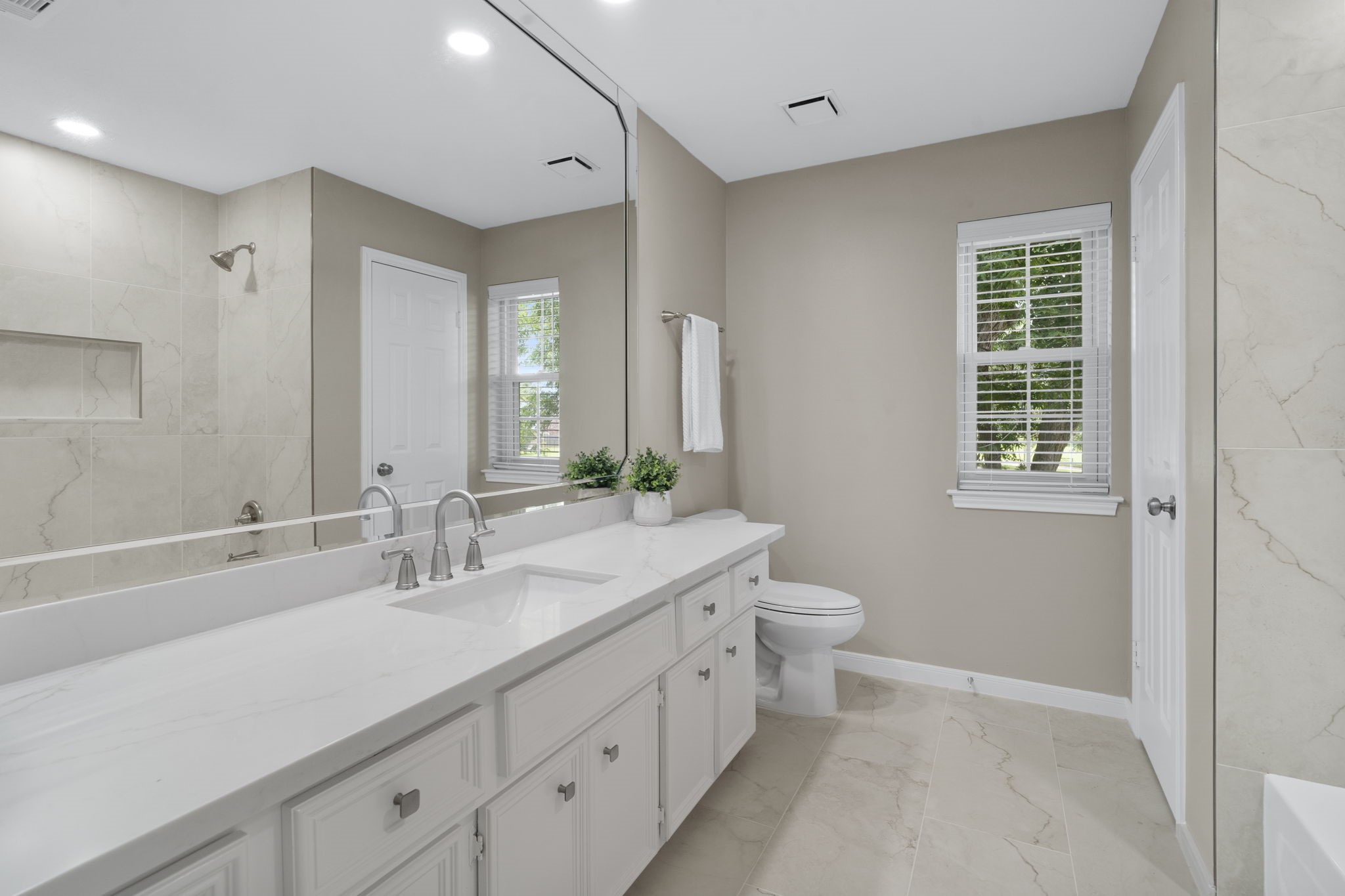 The updated secondary bath features a long vanity quartz countertop and expansive mirror.