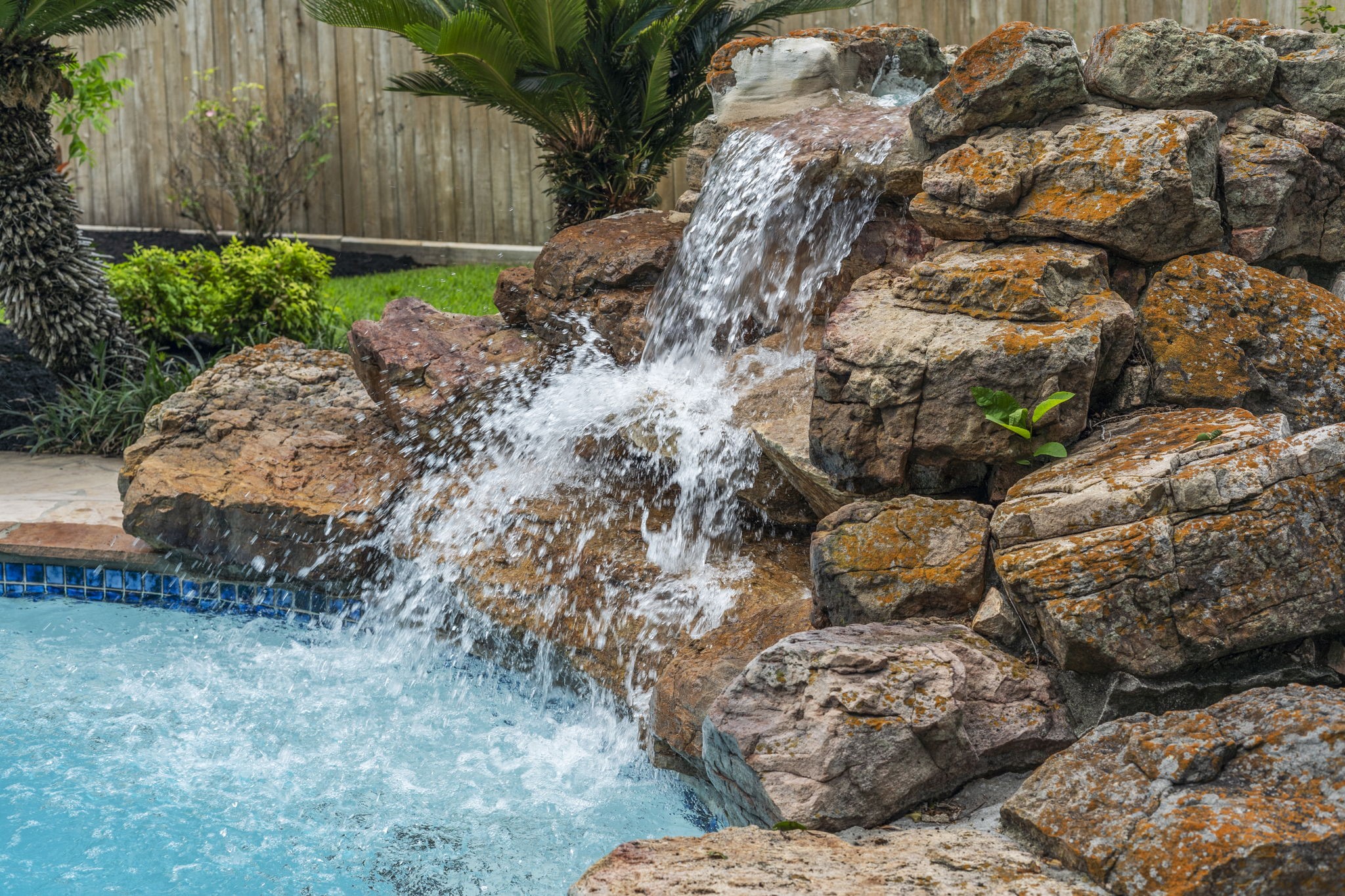 A dramatic rock waterfall adds movement & character to the pool, creating a beautiful focal point within the backyard. A dramatic rock waterfall adds movement & character to the pool, creating a beautiful focal point within the backyard.
