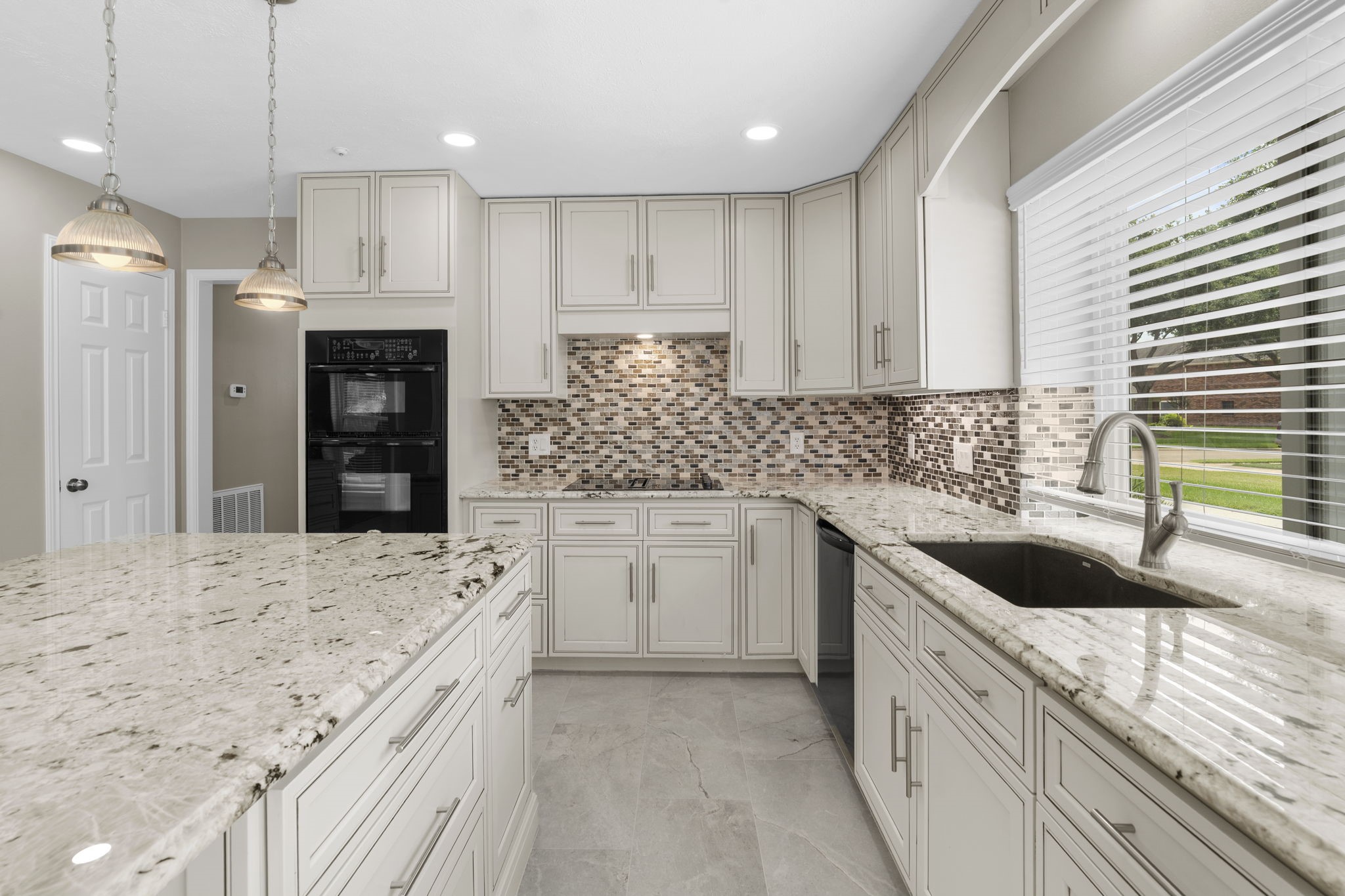 The kitchen offers abundant cabinetry, generous counter space & a large center island, complemented by granite surfaces, a mosaic tile backsplash & updated lighting. A large window over the sink fills the space with natural light.