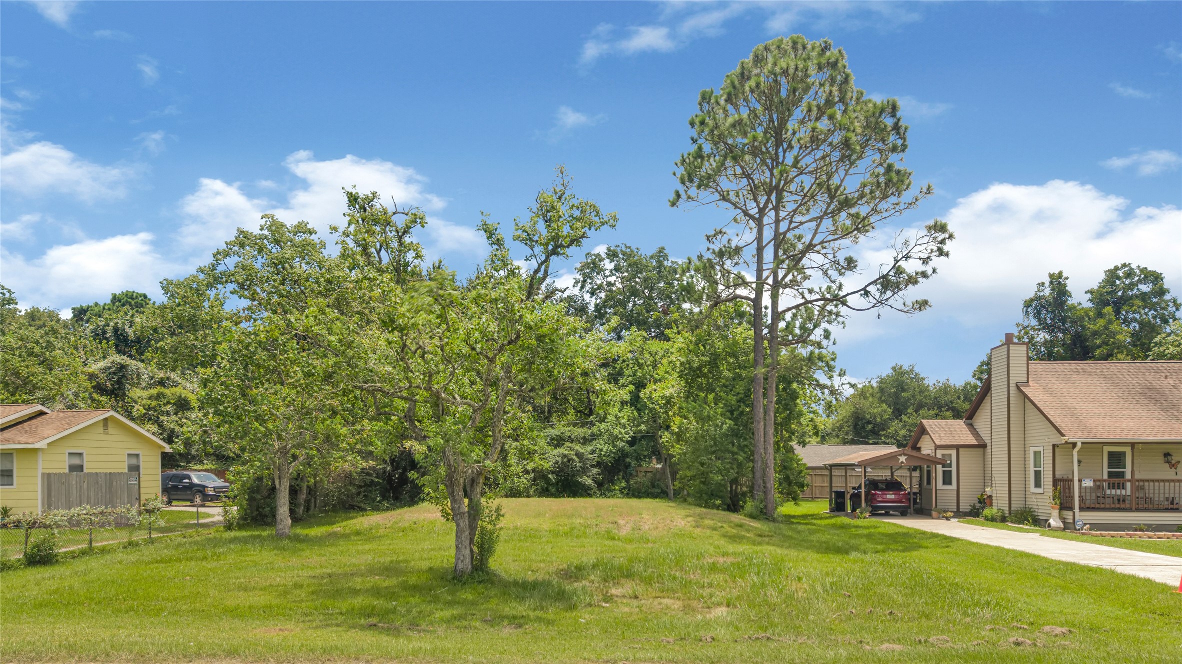 Spacious lot nestled between charming homes, featuring mature trees and a lush, green lawn, perfect for building your dream home in a serene neighborhood.