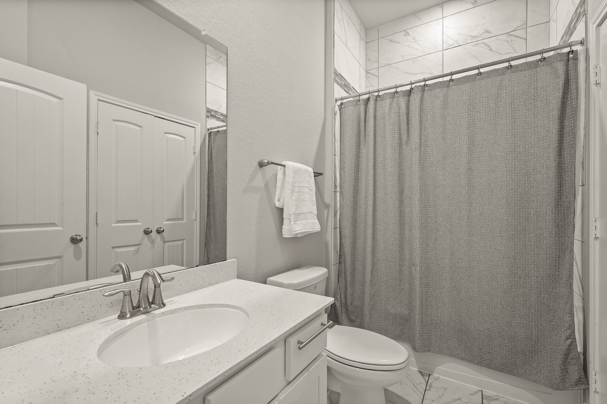 This beautifully appointed full bathroom features a crisp white vanity topped with a subtle quartz countertop, an under-mount oval sink, and a contemporary brushed nickel faucet. The tub/shower combination is framed by high-end, large-format marble-patterned wall tile.