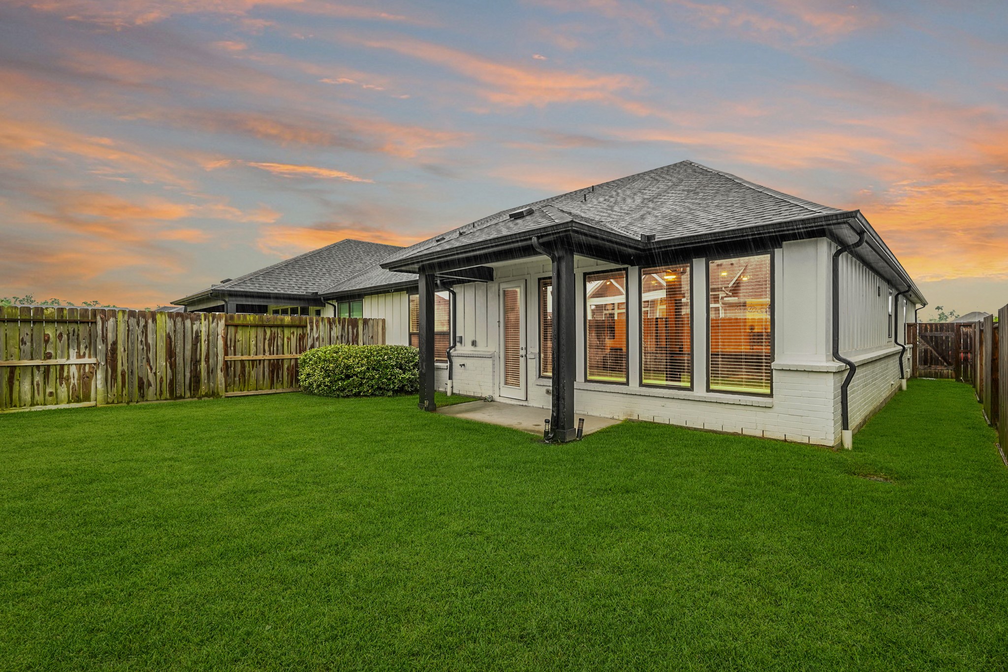 A beautiful perspective of the property's exterior. The home opens directly onto a covered back patio area, looking out over a generous expanse of green grass.