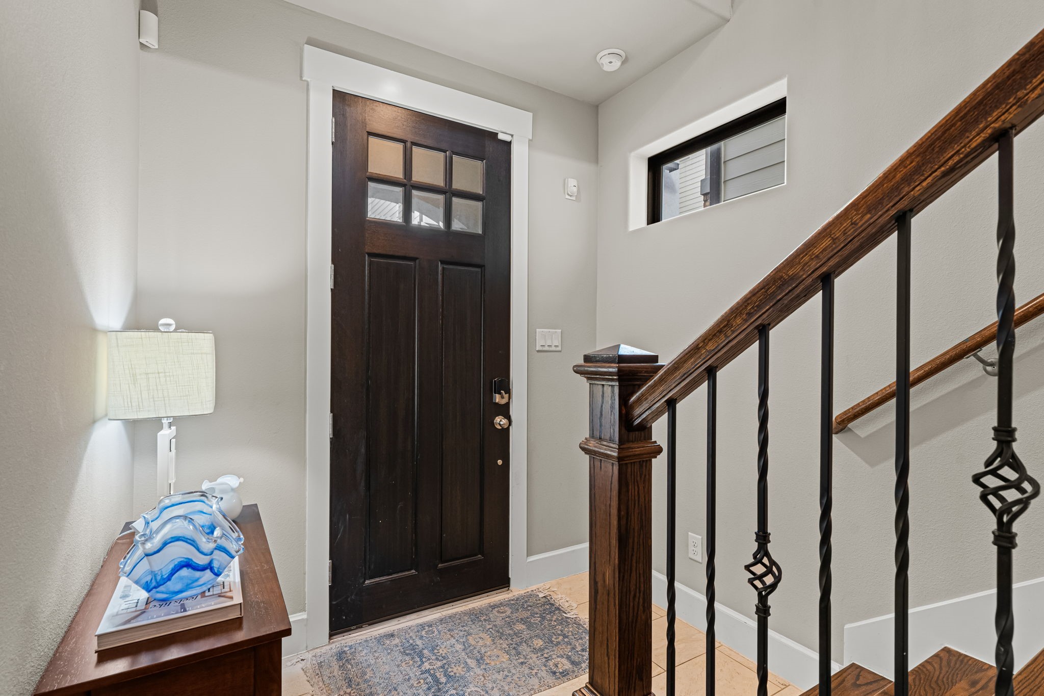 Daylight filters through the transom above the front door, illuminating a welcoming pocket of the foyer. A warm wood handrail and decorative ironwork carry the home's traditional detailing through the entry.