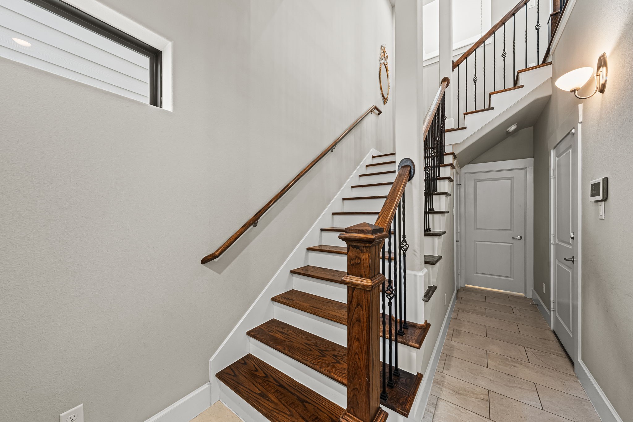 Rich wood treads and intricate iron balusters distinguish the foyer's beautifully detailed staircase. Pale tile and crisp white trim keep the entrance bright and composed.