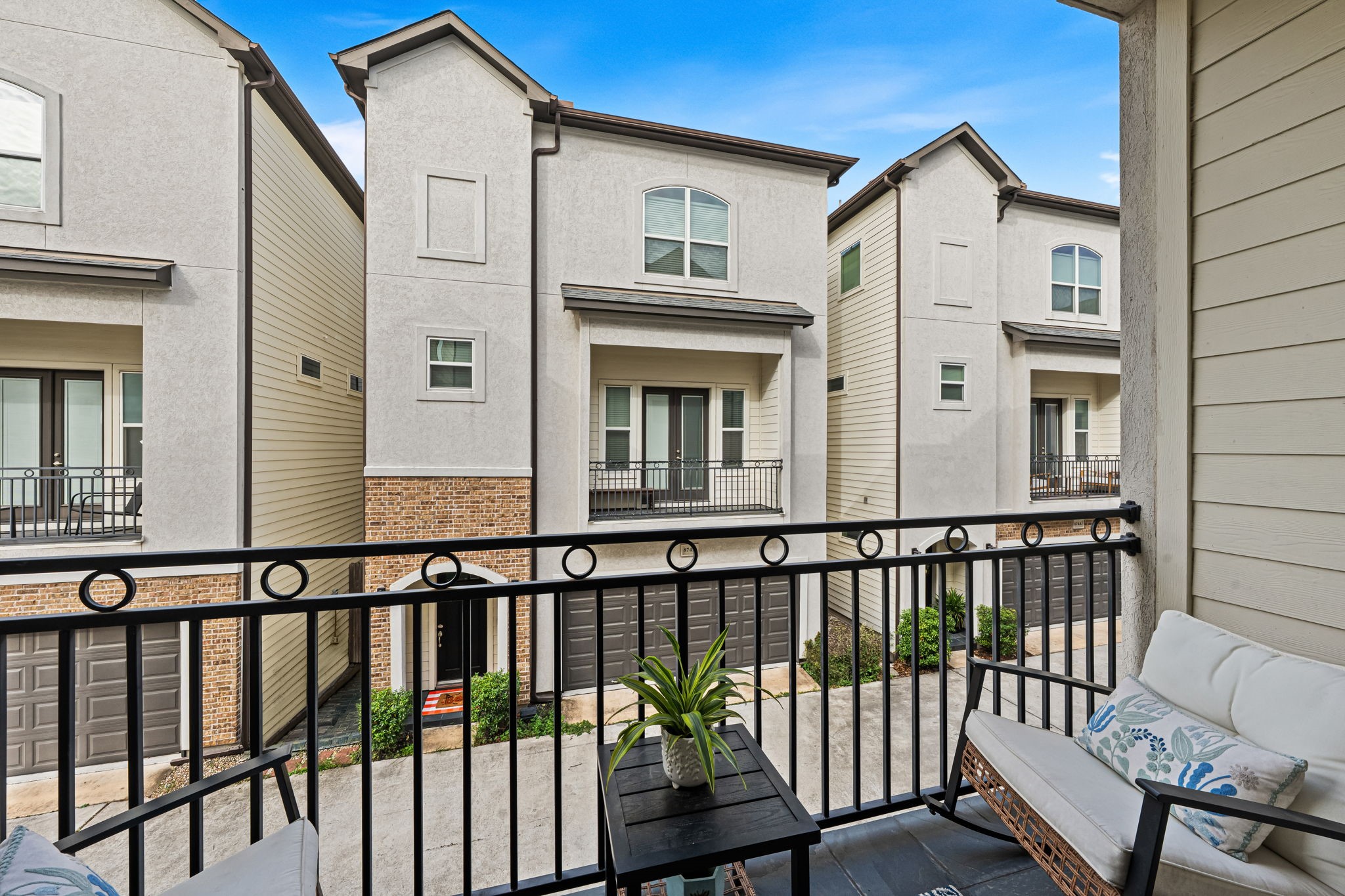 The covered balcony offers a sheltered perch for morning coffee or a pause at sunset. Dark metal railings frame the outlook across the neighboring homes.
