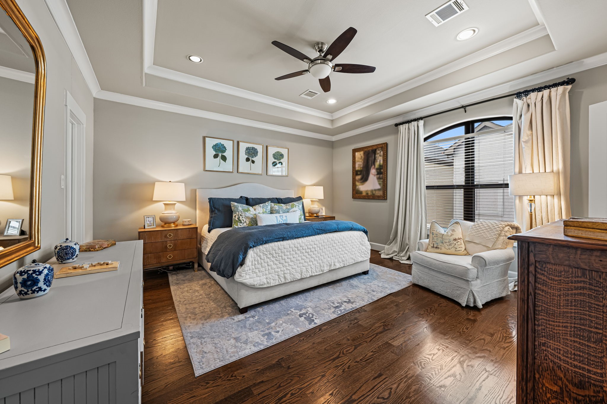 A beautifully recessed tray ceiling crowns the primary bedroom, where warm hardwoods meet a serene neutral palette. Broad windows fill this private retreat with soft natural light.
