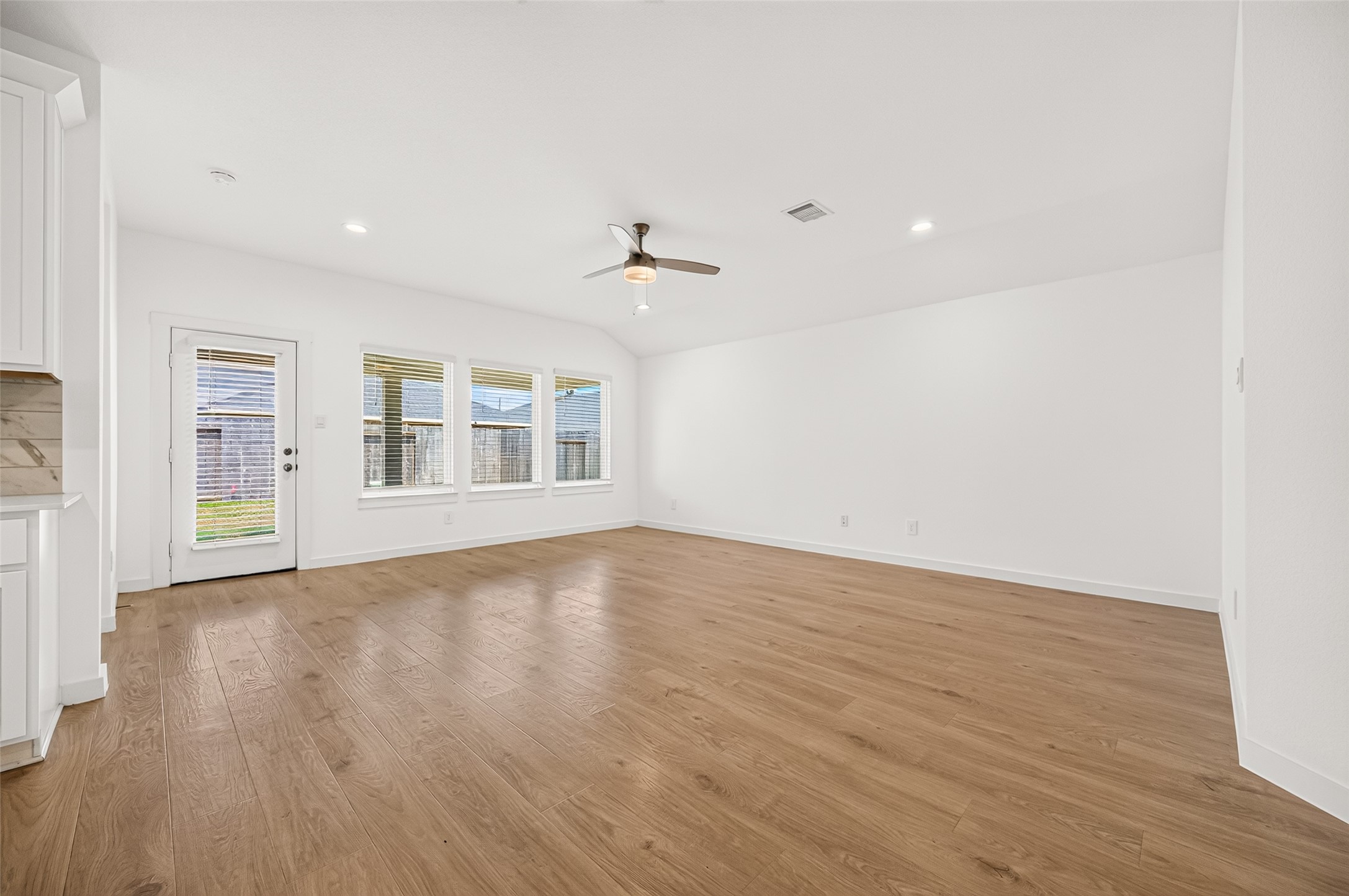 Wall of windows in the family room for natural lighting. Ceiling fan, mini blinds and recessed lighting. Primary bedroom to the left in the back of the home.
