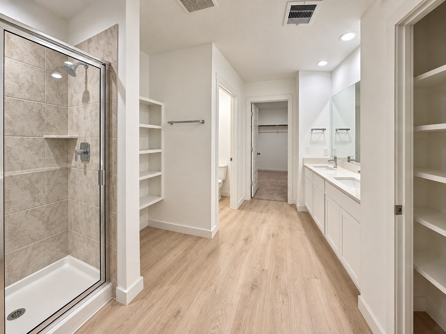 Primary bathroom suite with double sinks, walk in shower, linen closet, shelving and a powder room with privacy door.